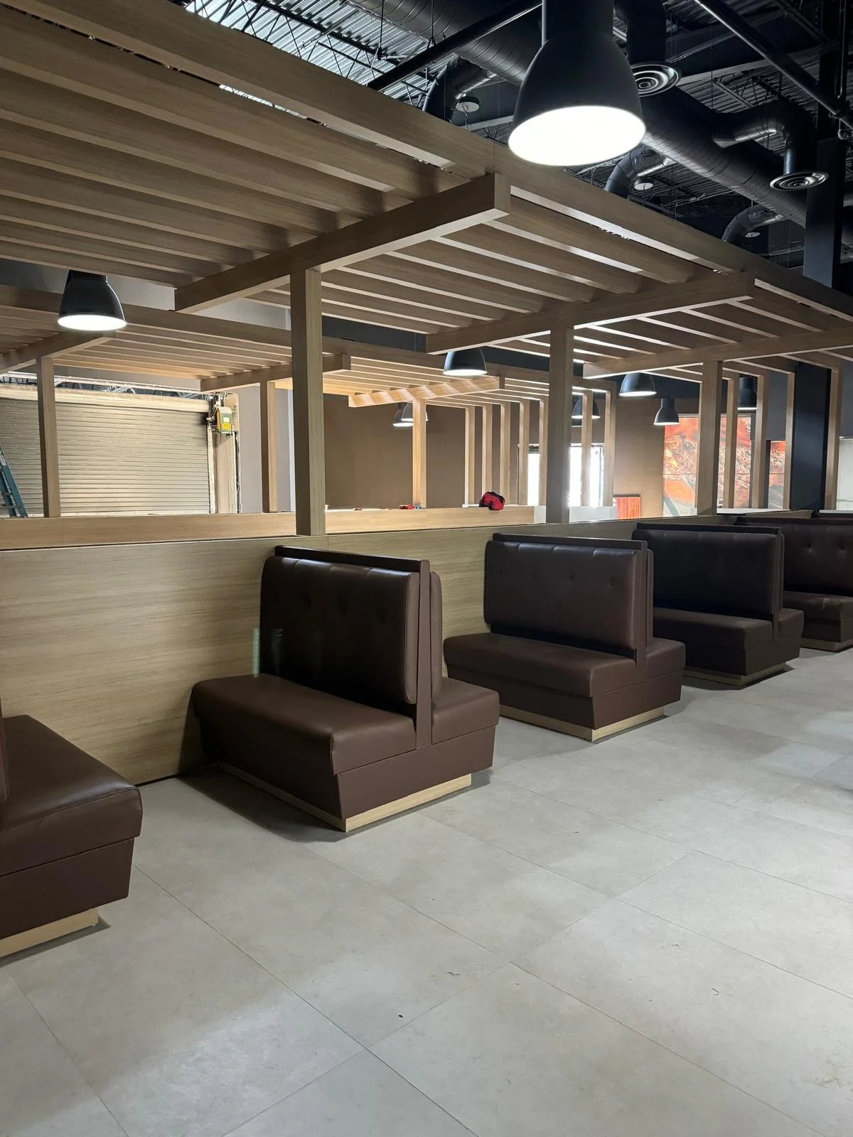 Interior of a commercial space under construction, with booth seating and wooden framework for a divider or wall, modern lighting, and exposed ceiling ducts.