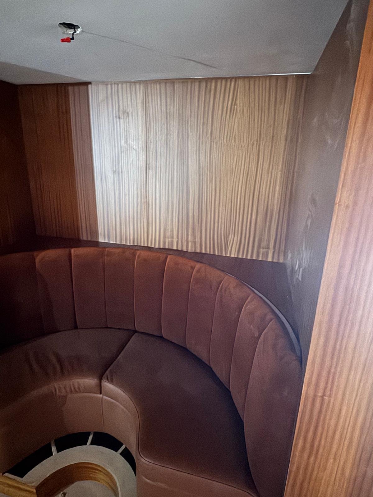 Interior of a room with bar seating, rounded brown leather booth, wood panel walls, and an unfinished ceiling with a hanging electrical wire.