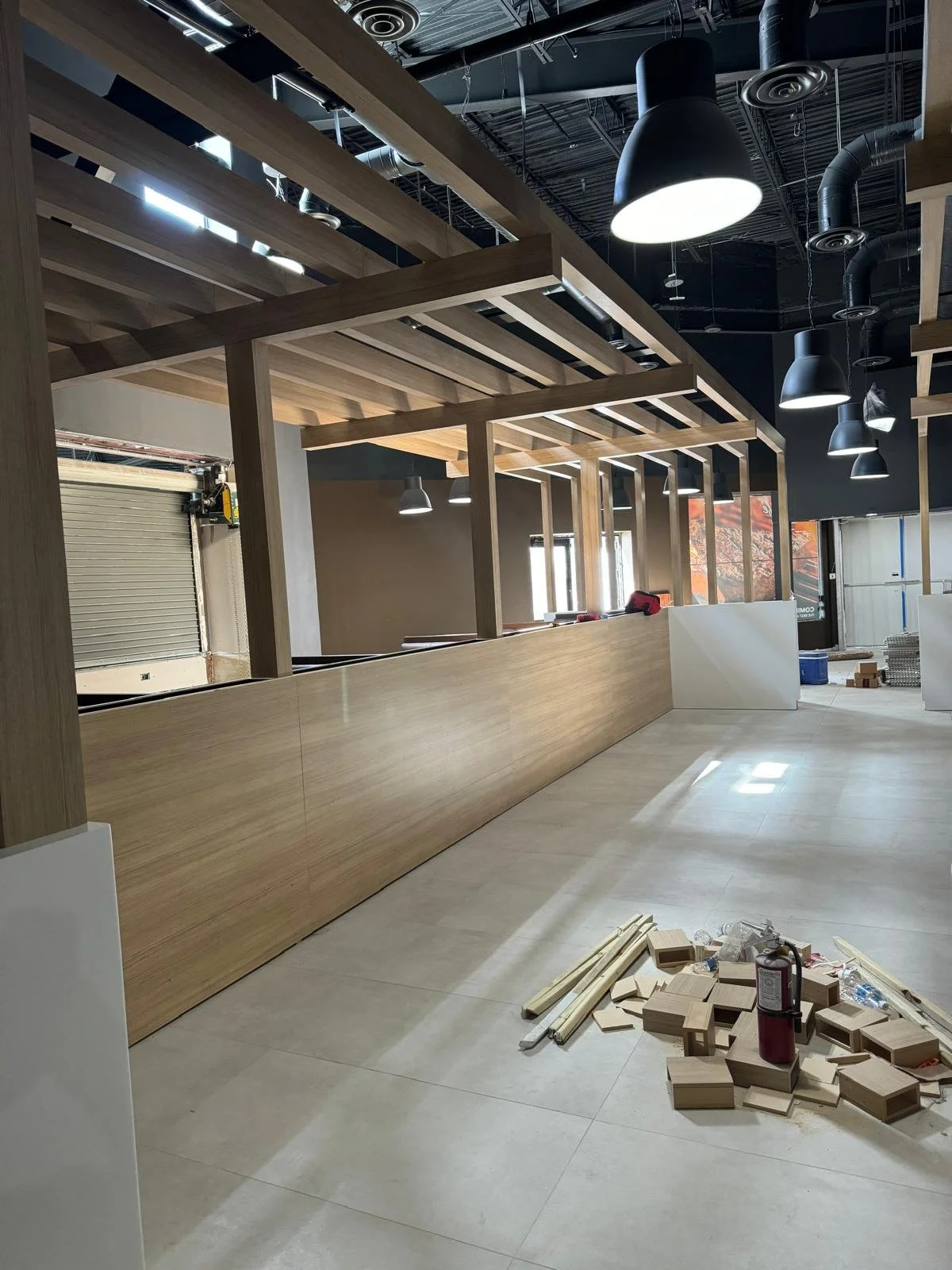 Interior of a building under construction with wood framing, hanging black pendant lights, and construction materials on the floor.