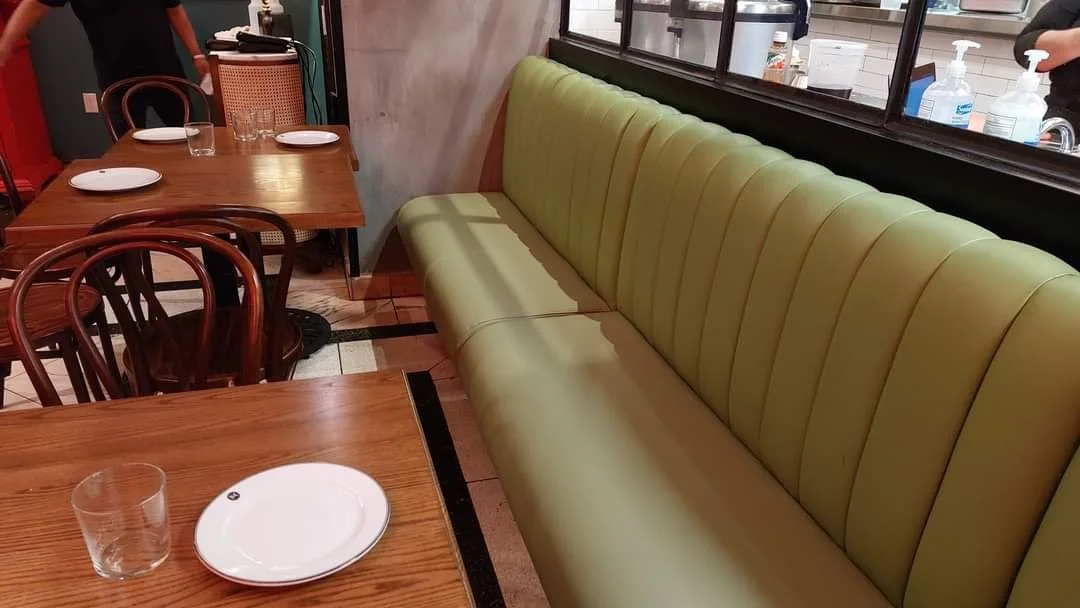 Empty green upholstered booth seat with wooden tables set with plates and glasses in a restaurant.
