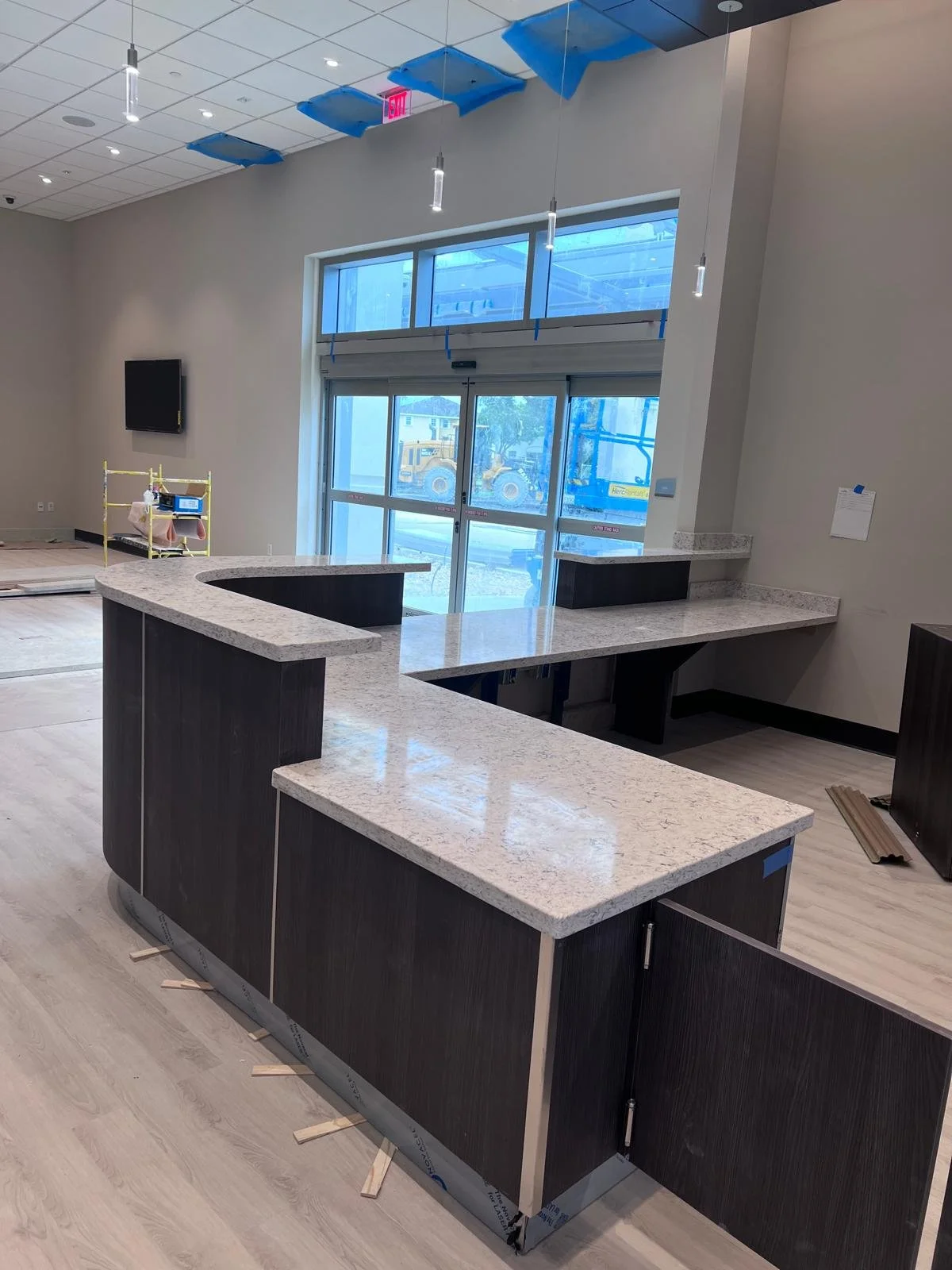 Interior view of a modern commercial space under construction with a curved granite counter, large windows, and construction equipment outside.
