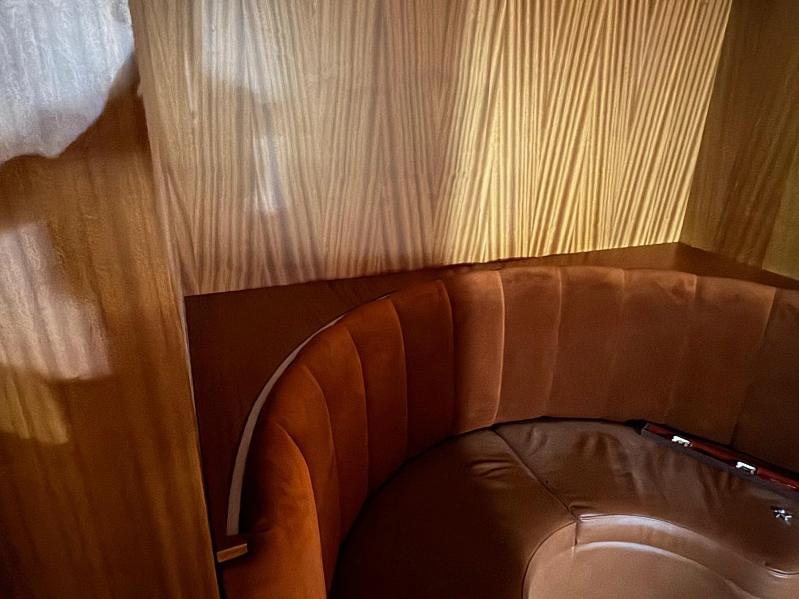 A curved leather booth seating area with a wooden wall and a beige curtain or drapery in the background.