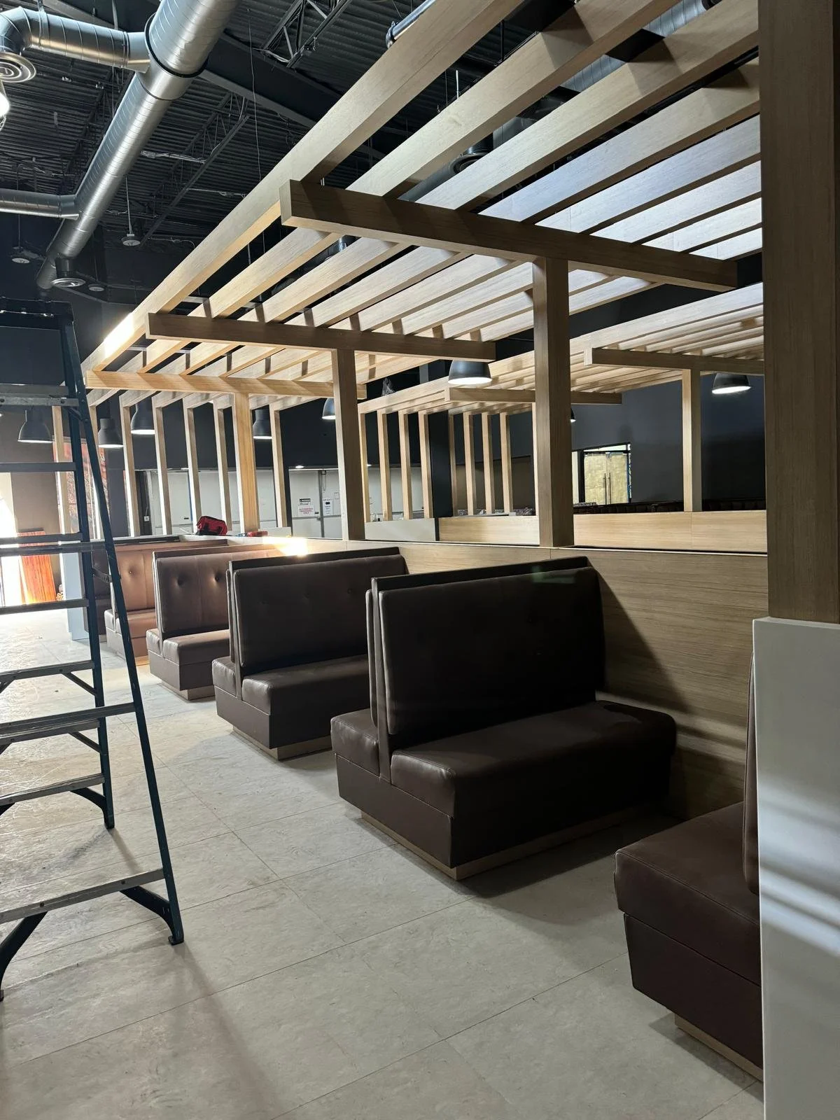Interior of a restaurant under construction with booths, wood accents, and an unfinished ceiling with visible ductwork.