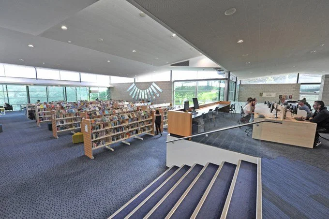 Modern library interior with bookshelves, a reading area, and a spiral staircase.