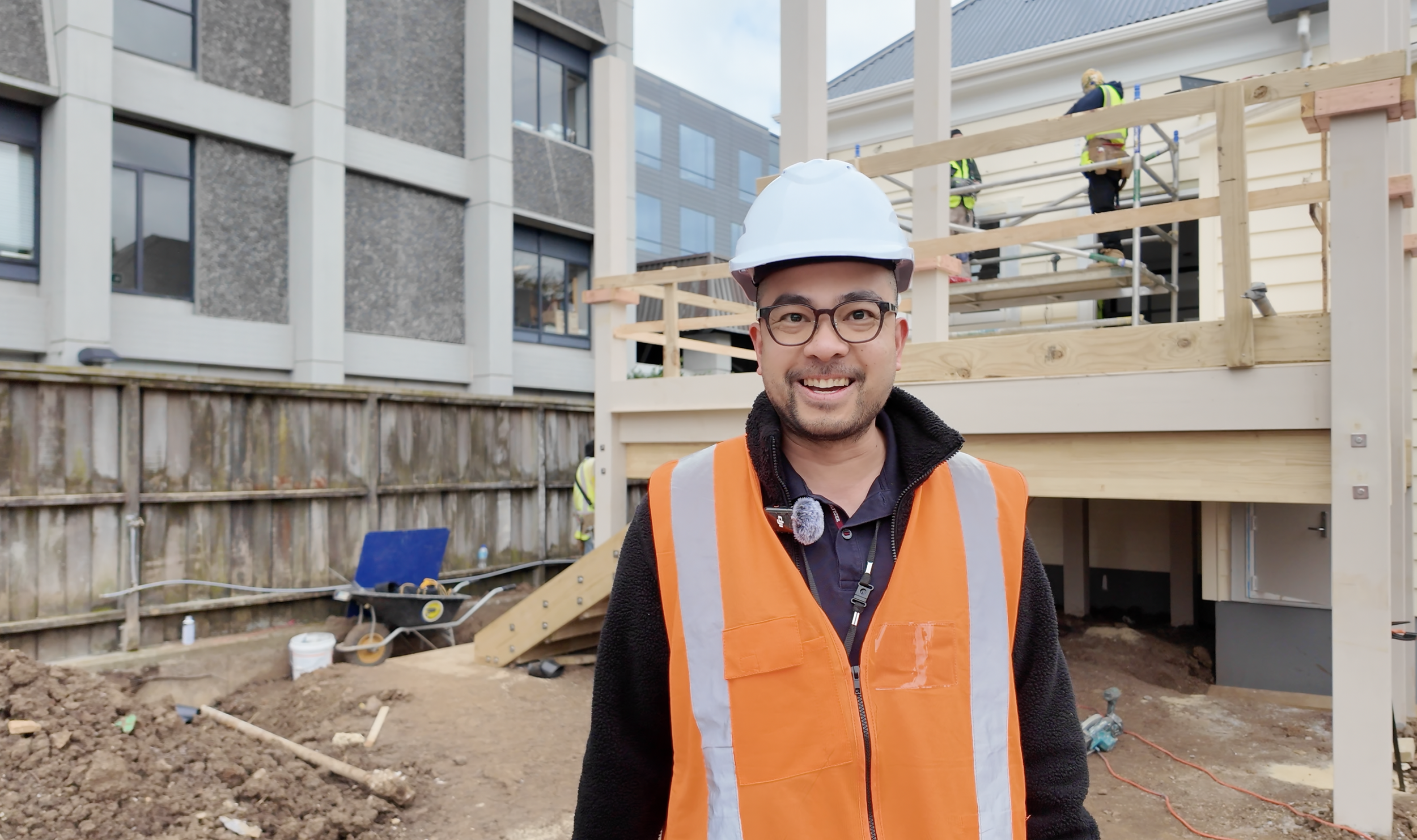 Hampton Jones structural engineer wearing safety helmet and orange vest standing in a construction site with building under construction in the background.