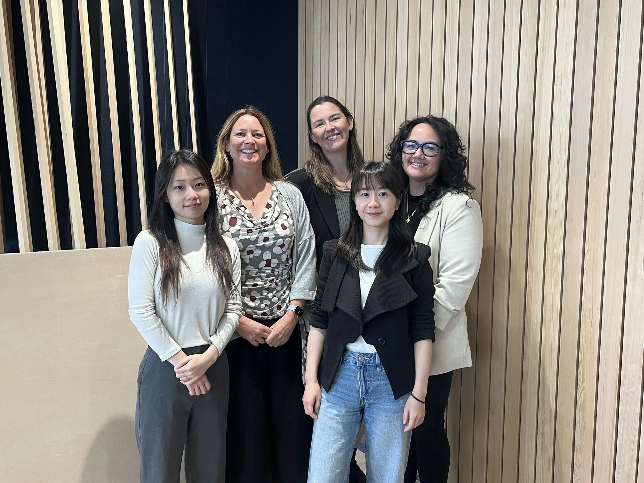 TSB bank fit out project, hampton jones consultants posing together indoors, smiling at the camera, standing in front of a wooden panel wall.