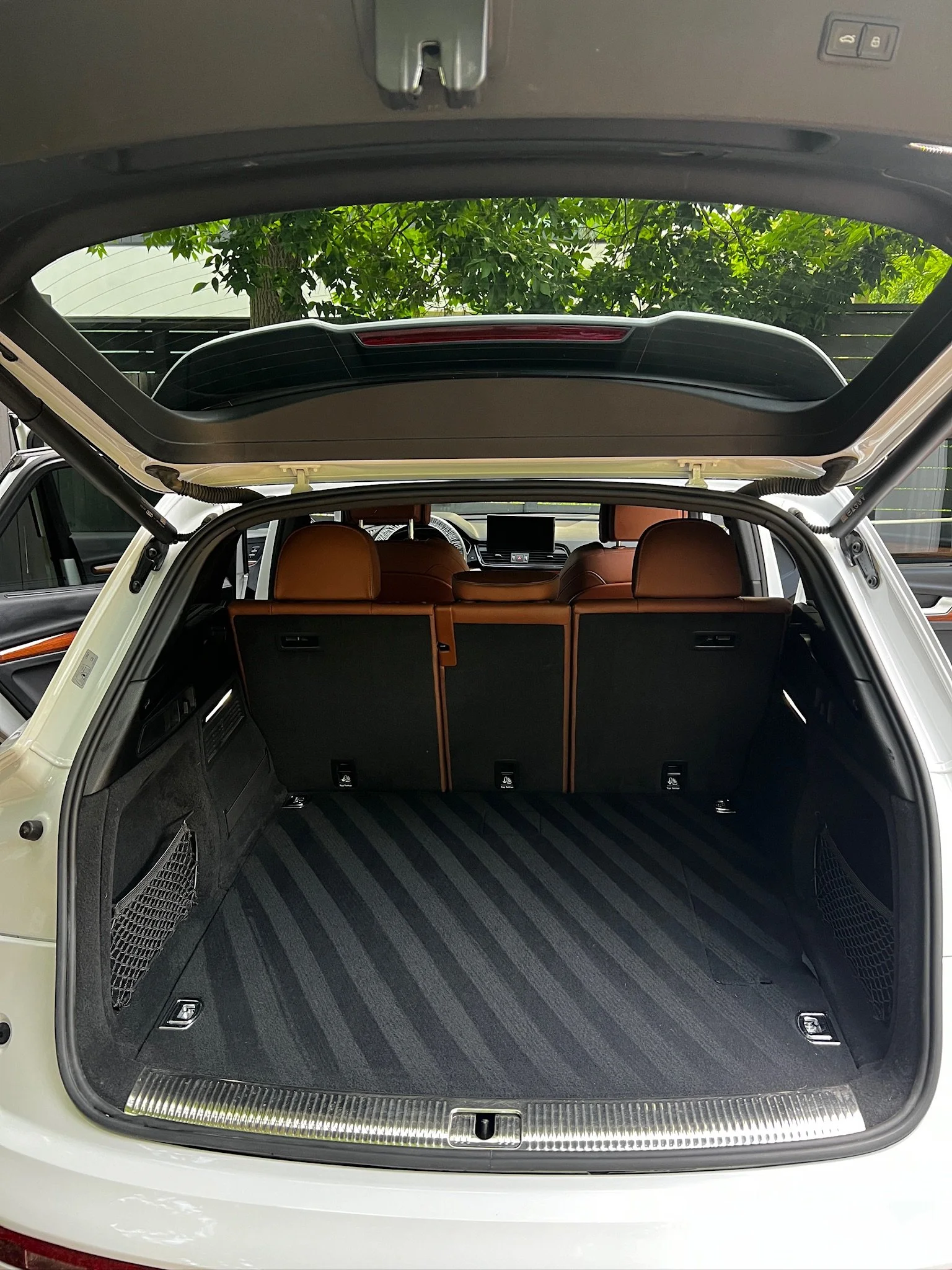 Open trunk of a luxury SUV showing black carpeted cargo space, brown leather back seats, and side storage nets.