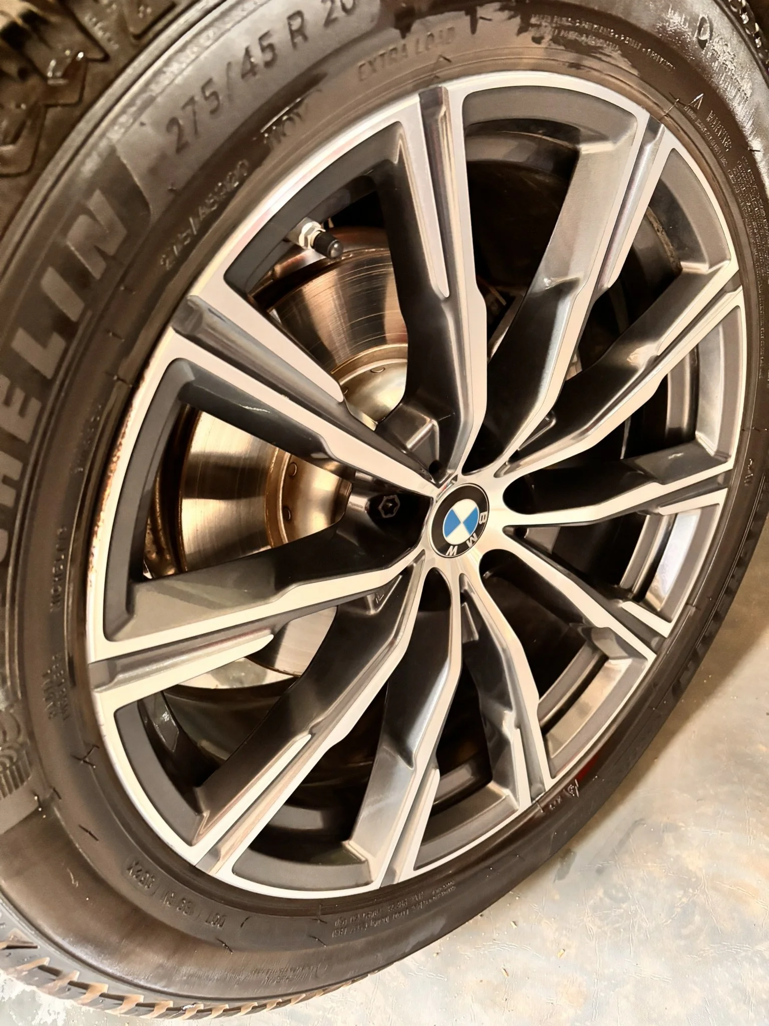 Close-up of a BMW car wheel with a metallic alloy rim and a black tire, showing detailed spokes and brand logo in the center.
