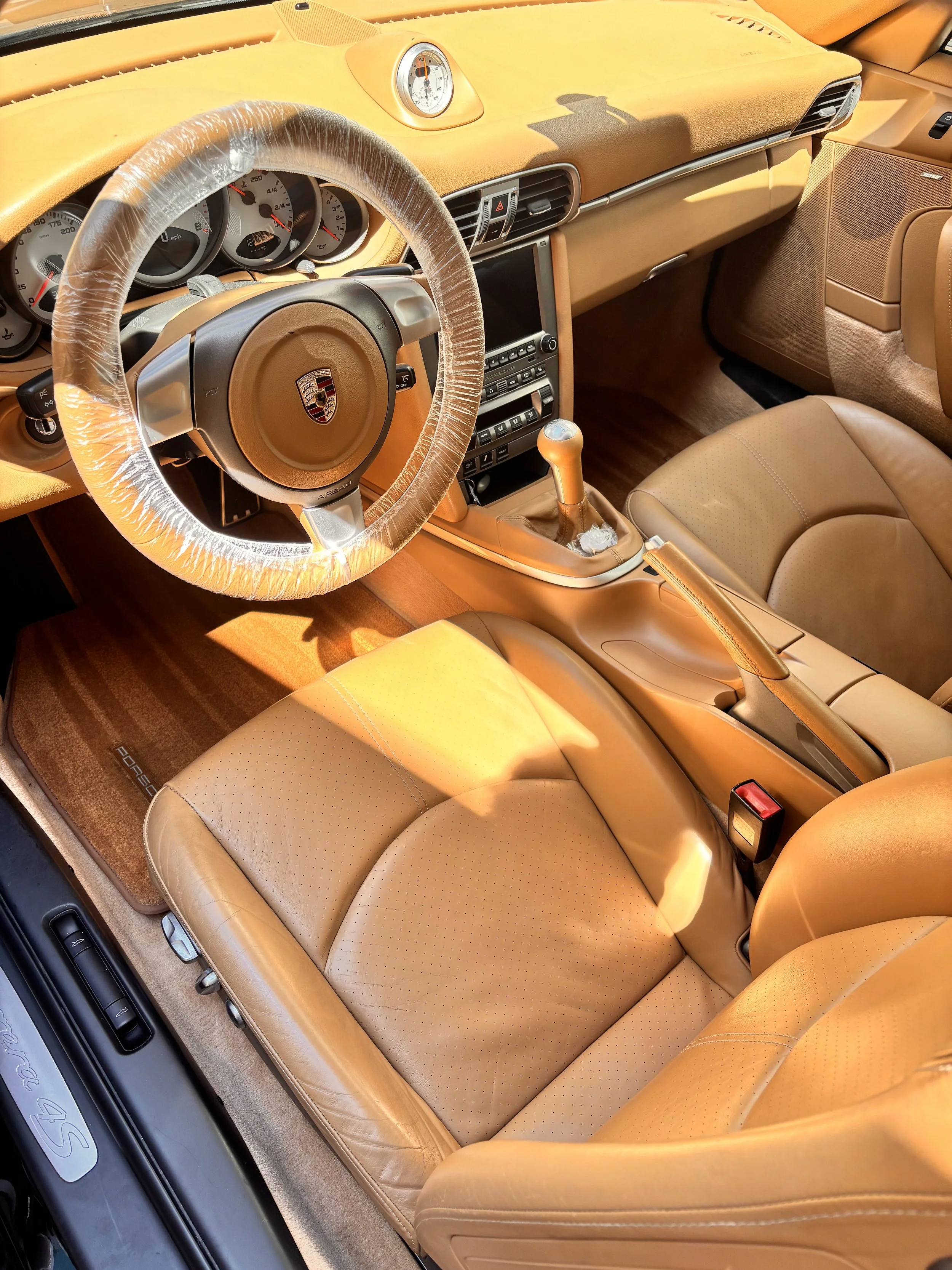 Interior of a tan-colored Porsche sports car showing the steering wheel, dashboard, gear shift, and front seats.