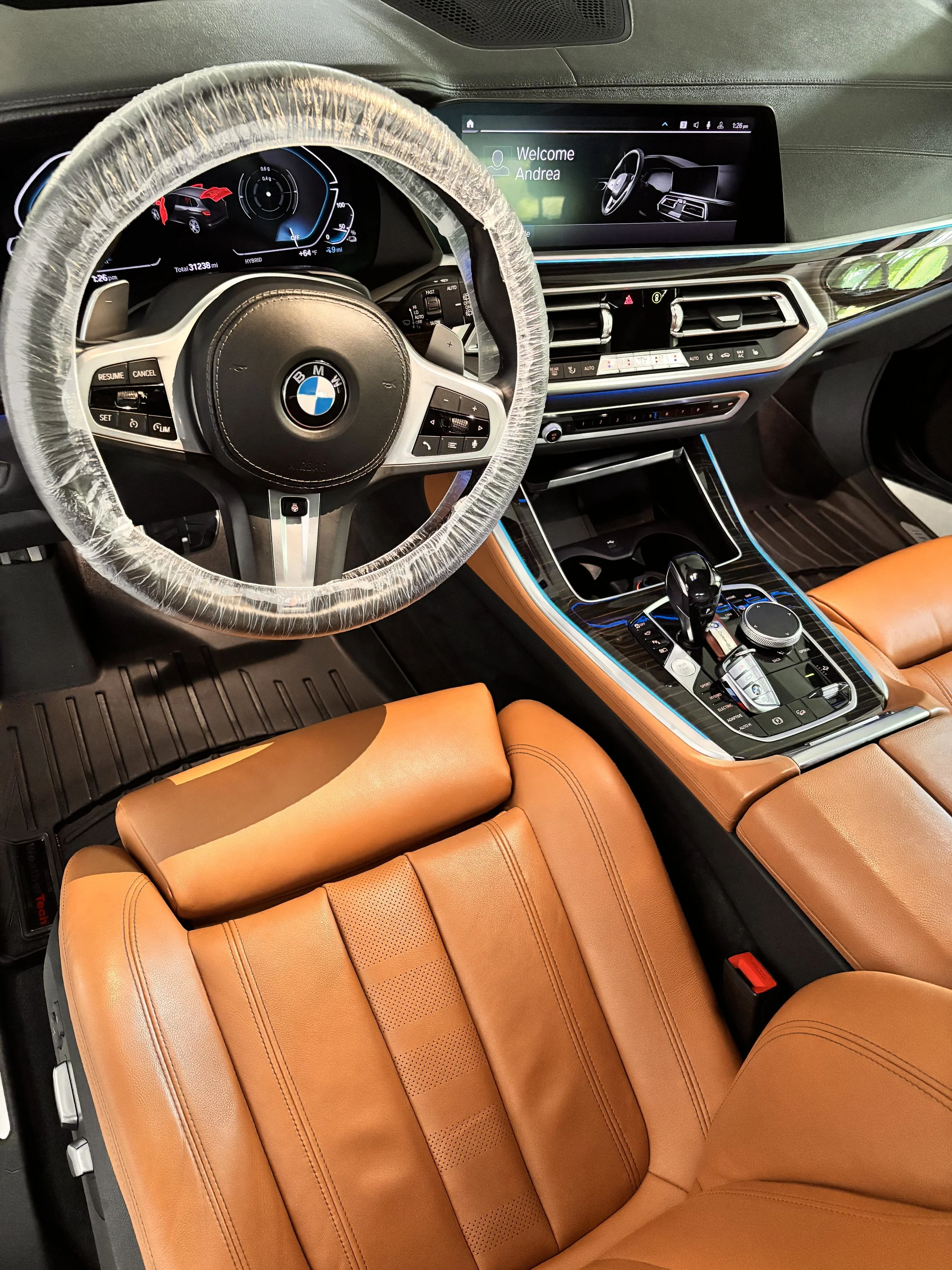 Interior of a BMW vehicle showing the dashboard, steering wheel, and tan leather seats.