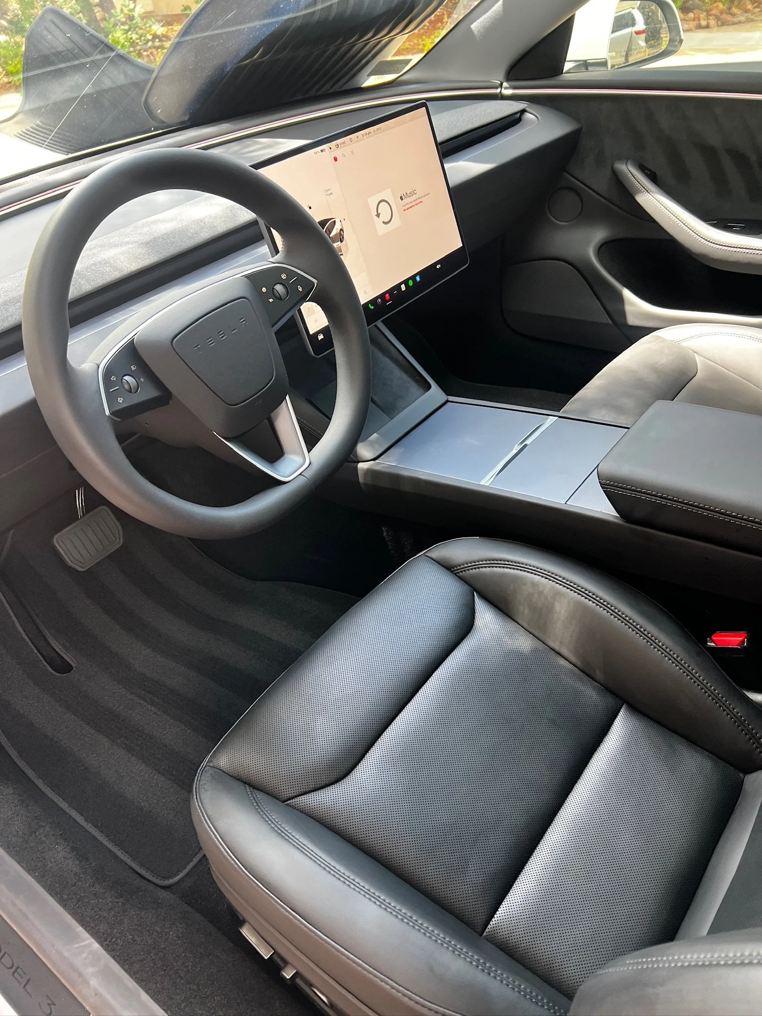 Interior of a modern vehicle focusing on the driver's seat and dashboard, featuring a large touchscreen display, a steering wheel, and leather seats.