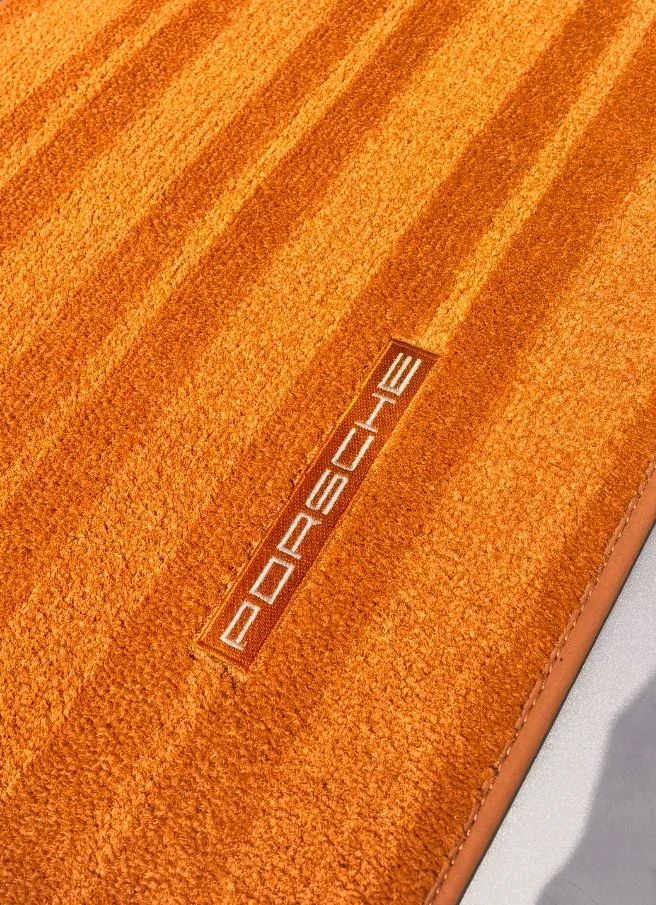 Close-up of an orange Porsche branded carpet or fabric with the Porsche logo embroidered.