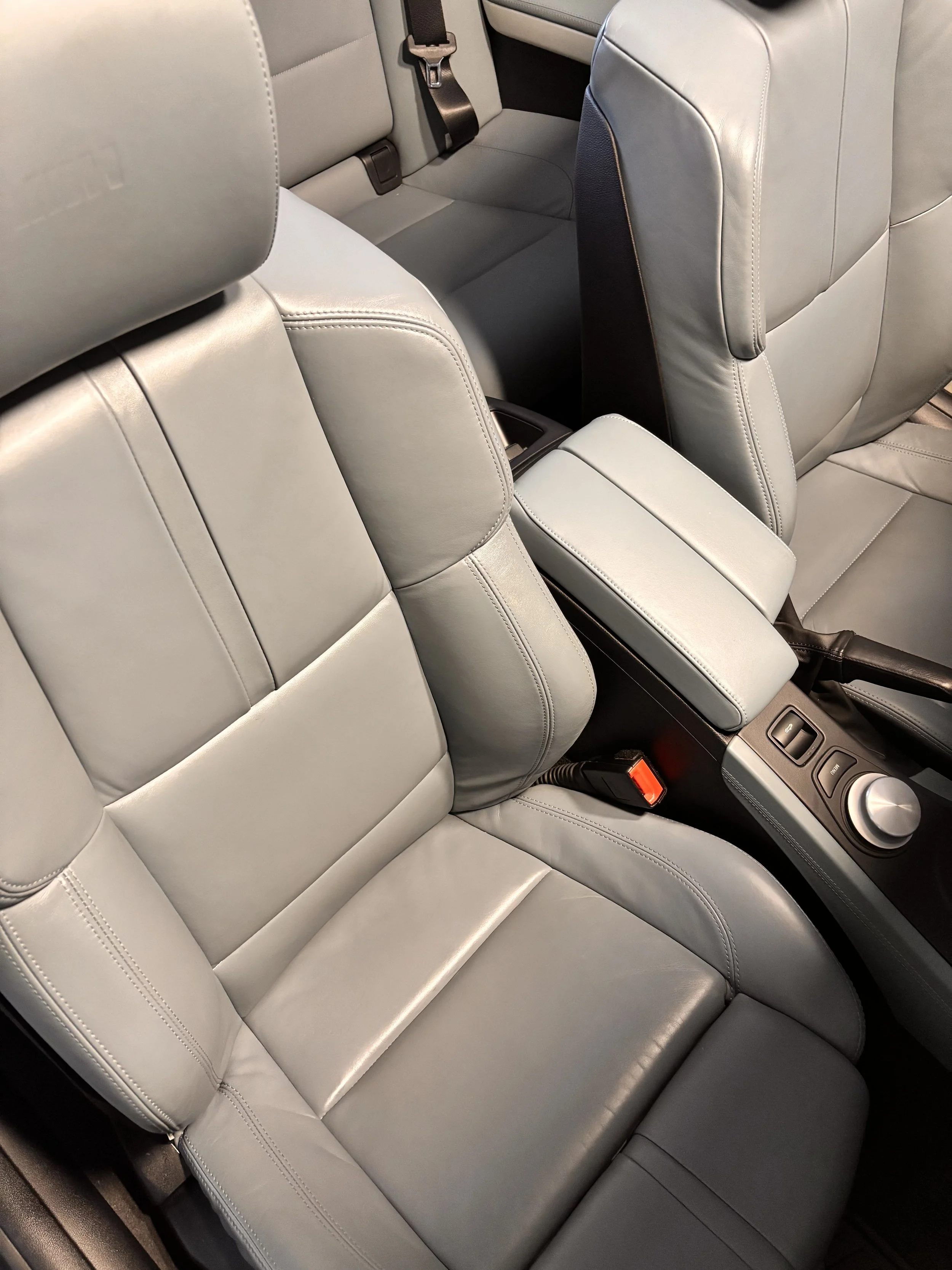 Front and back seats of a car with light gray leather upholstery, including a center armrest and minimalist controls on the console.
