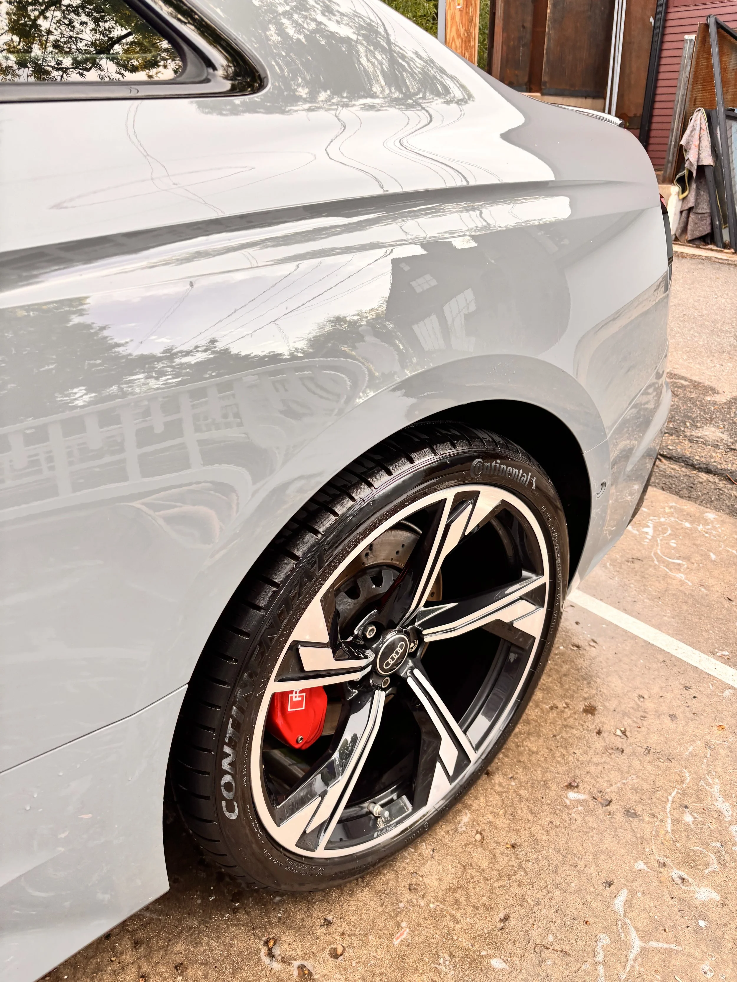 Close-up of the rear side of a silver Audi car showing the wheel with black and silver rim and red brake caliper.