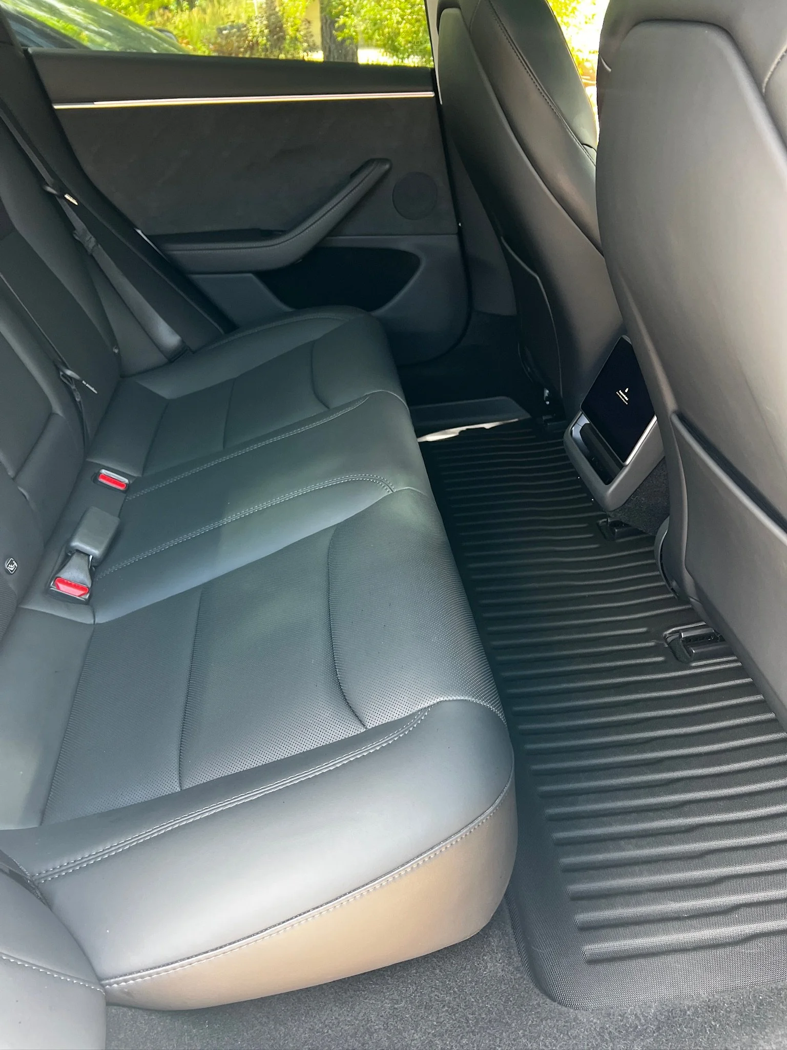 The back seat of a car with black leather seats, rear air vents, and a rubber floor mat.