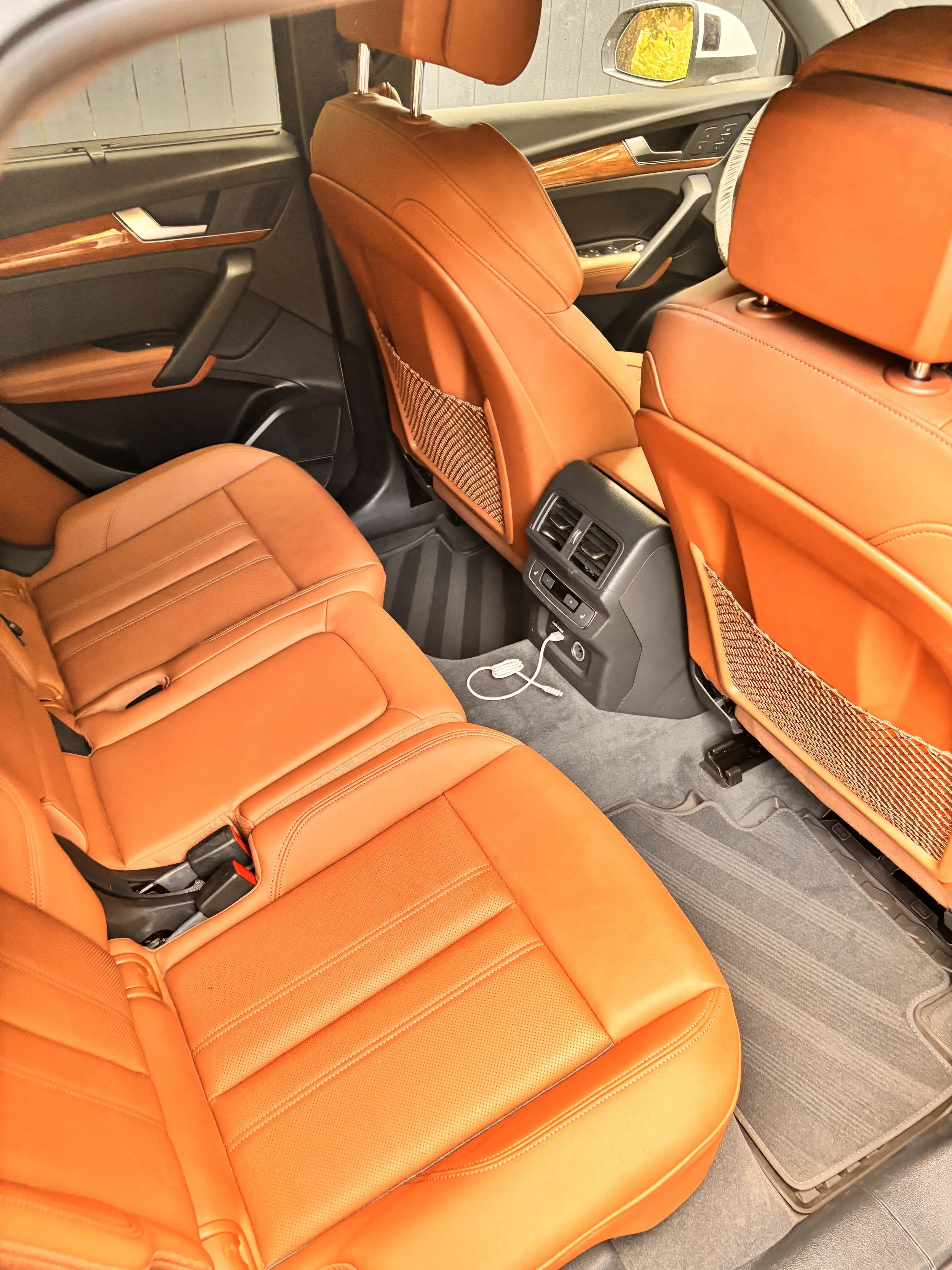 Interior of a car showing orange leather seats, the back of the driver and passenger seats, rear passenger seats, and floor mats.