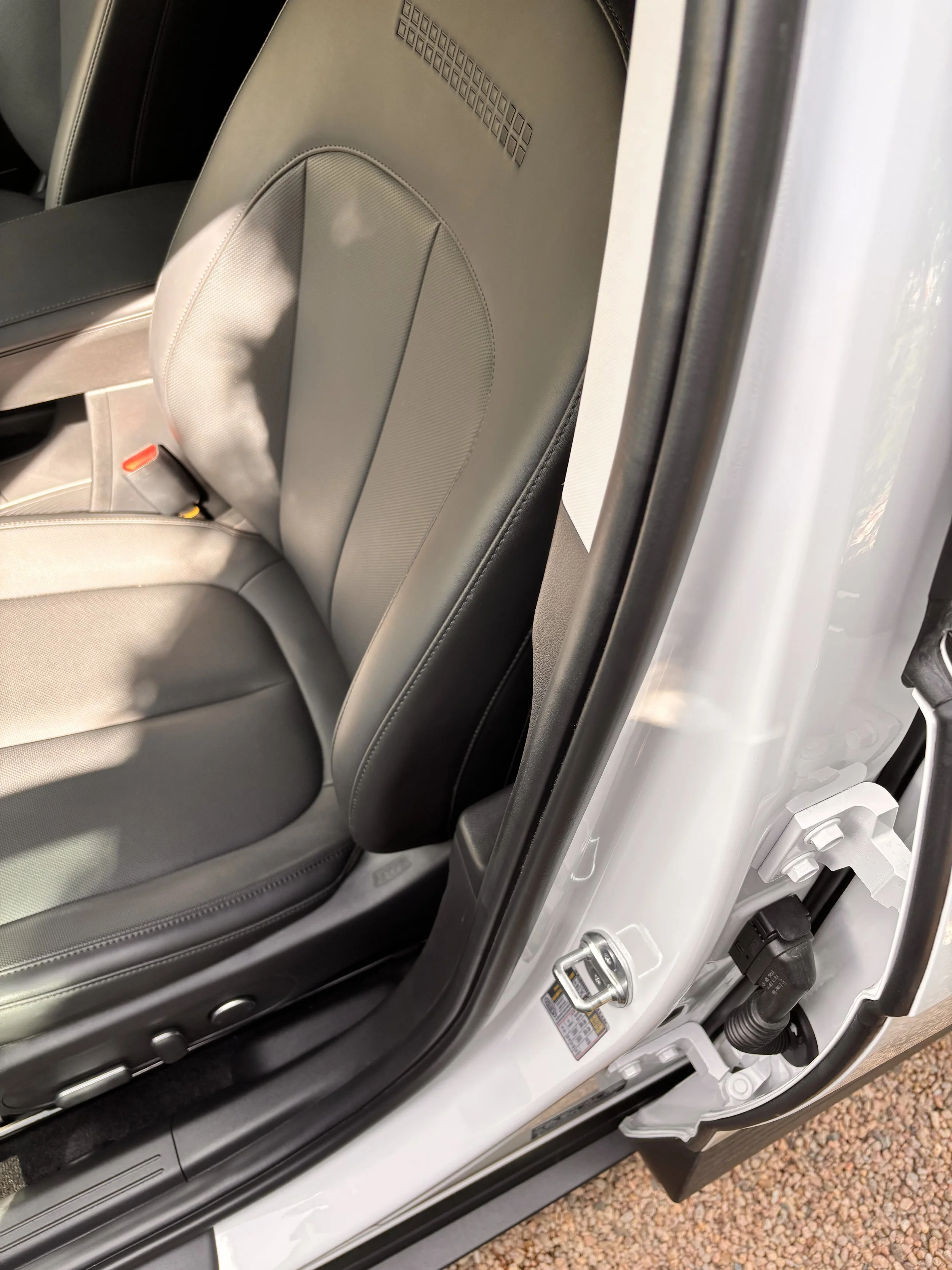 Interior of a car showing the front passenger seat and part of the door frame, with sunlight casting shadows on the seat.
