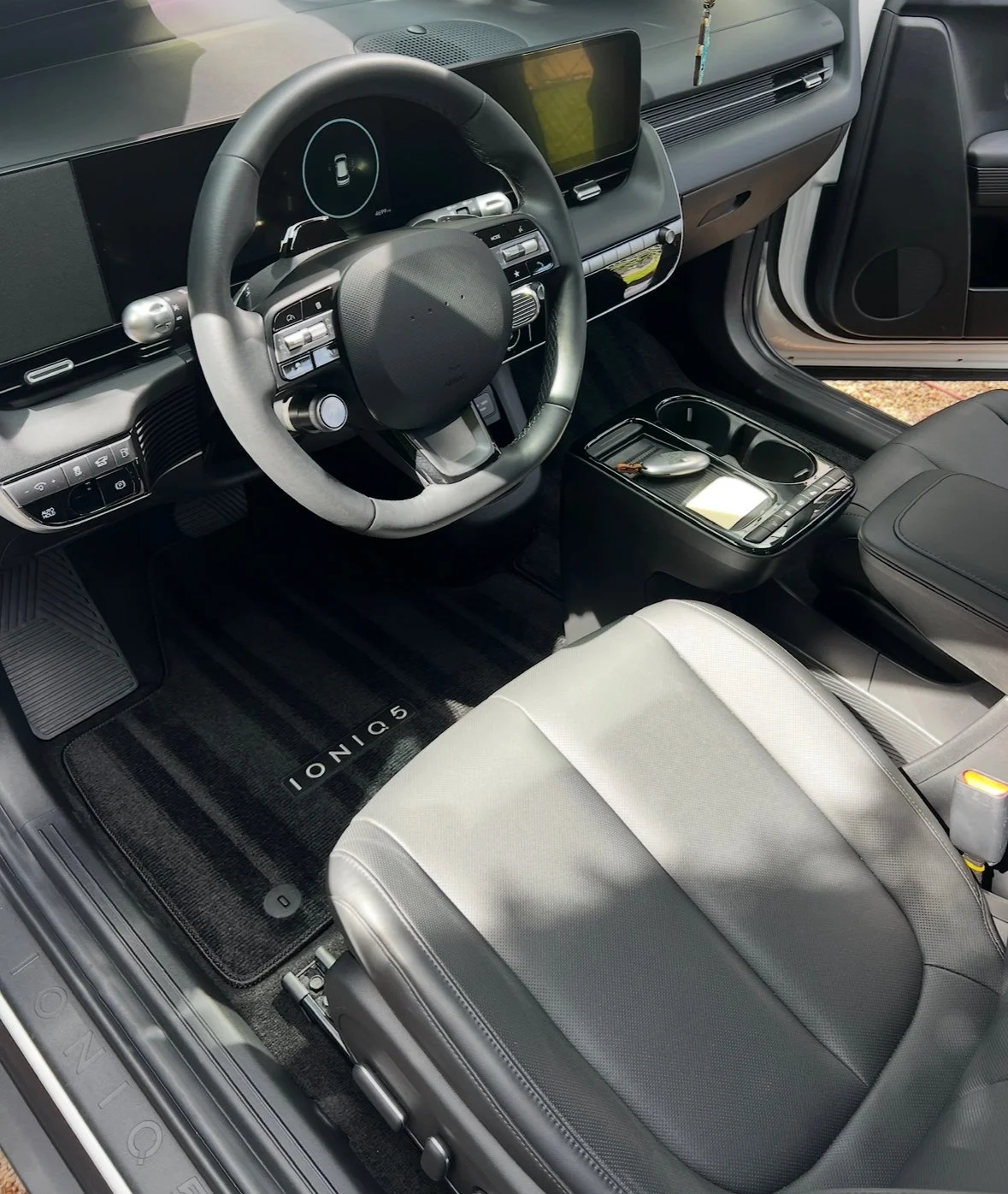 Interior of a modern car showing the dashboard, steering wheel, center console, and front seat with a black floor mat labeled 'IONIQ 5'.
