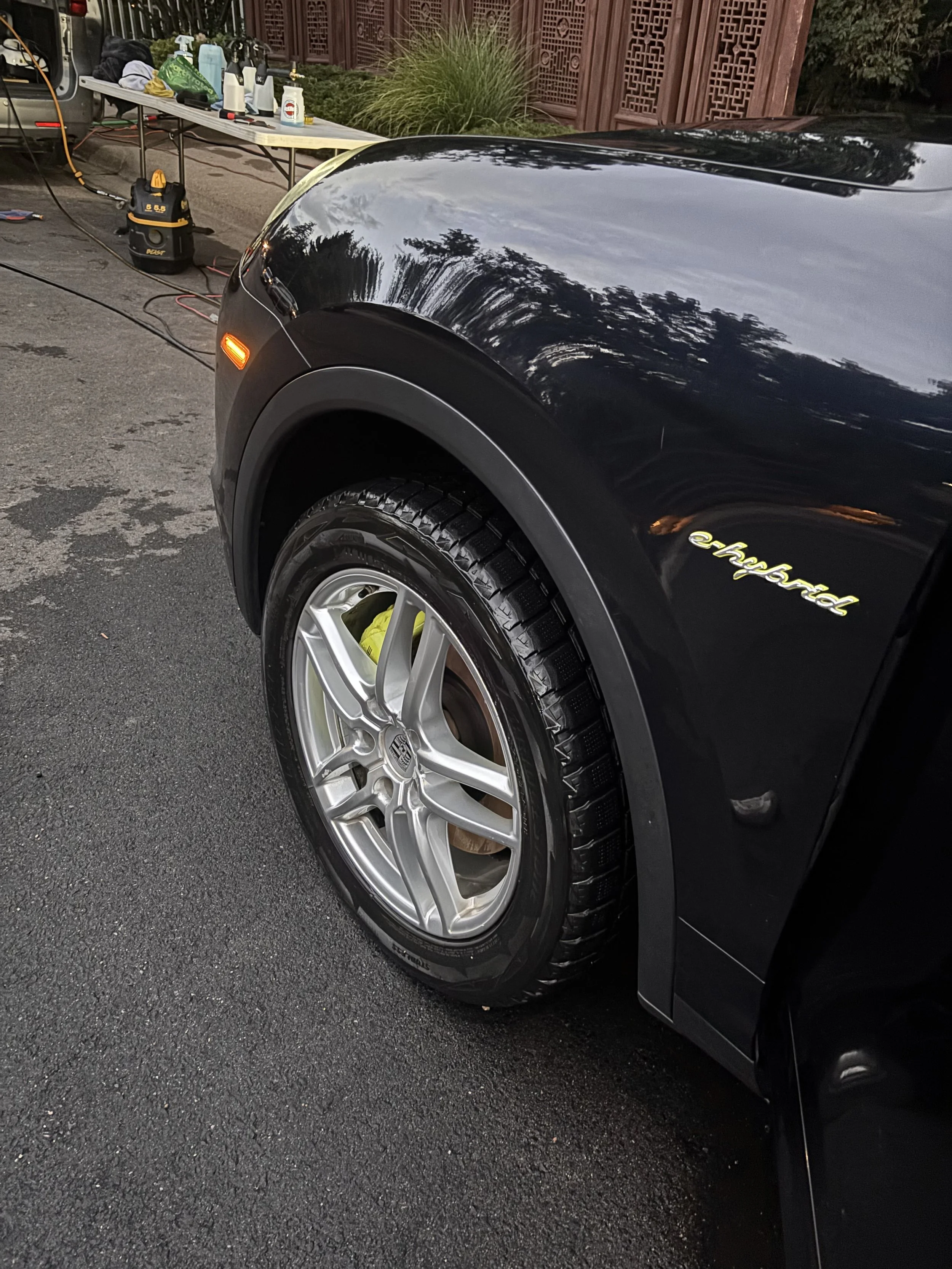 Close-up of the front part of a black electric car with the 'ehlers' badge, parked on an asphalt surface, with a table in the background holding cleaning supplies and equipment.