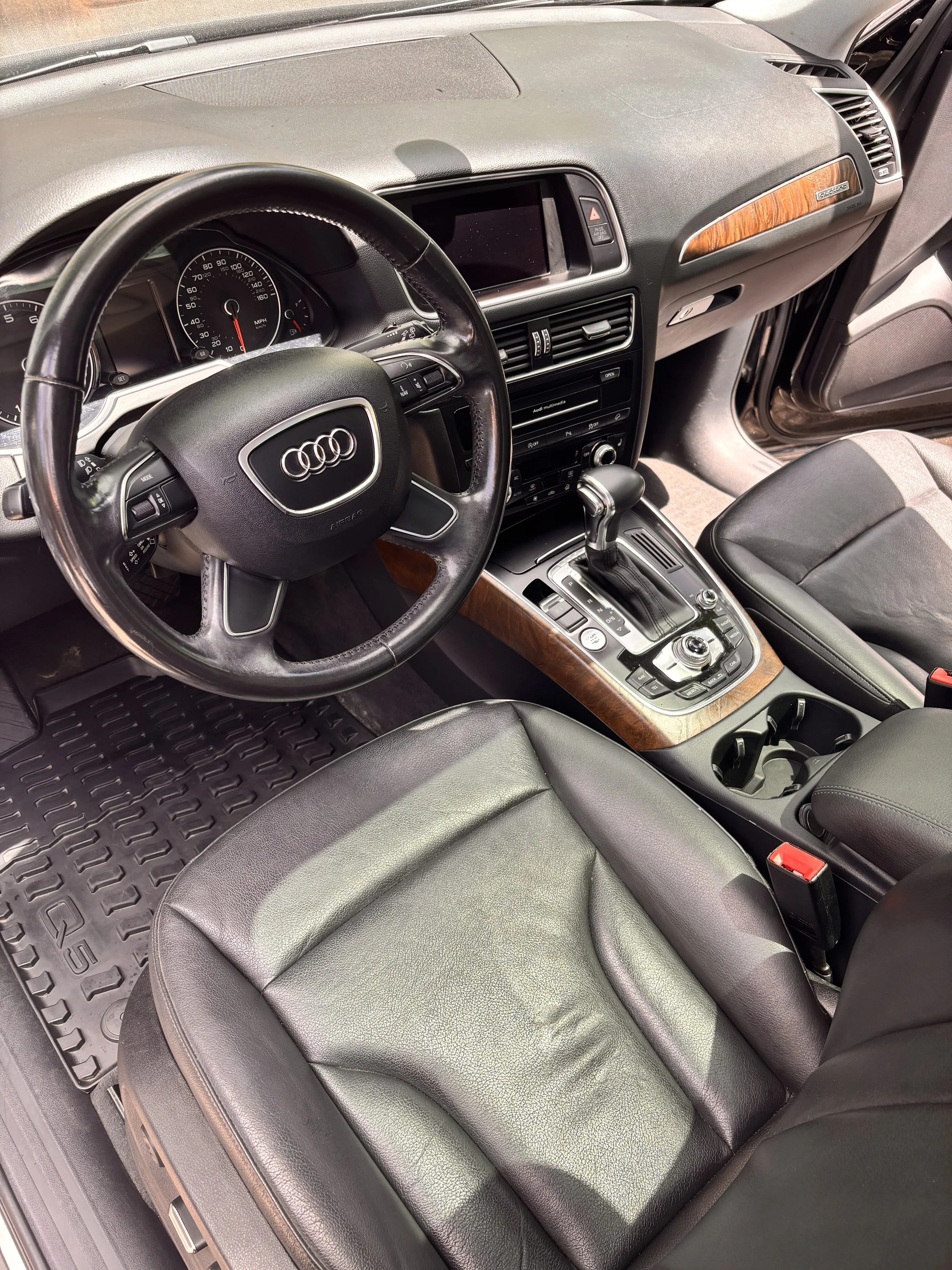 Interior of an Audi car showing the steering wheel, dashboard, gear shift, leather seats, and center console.