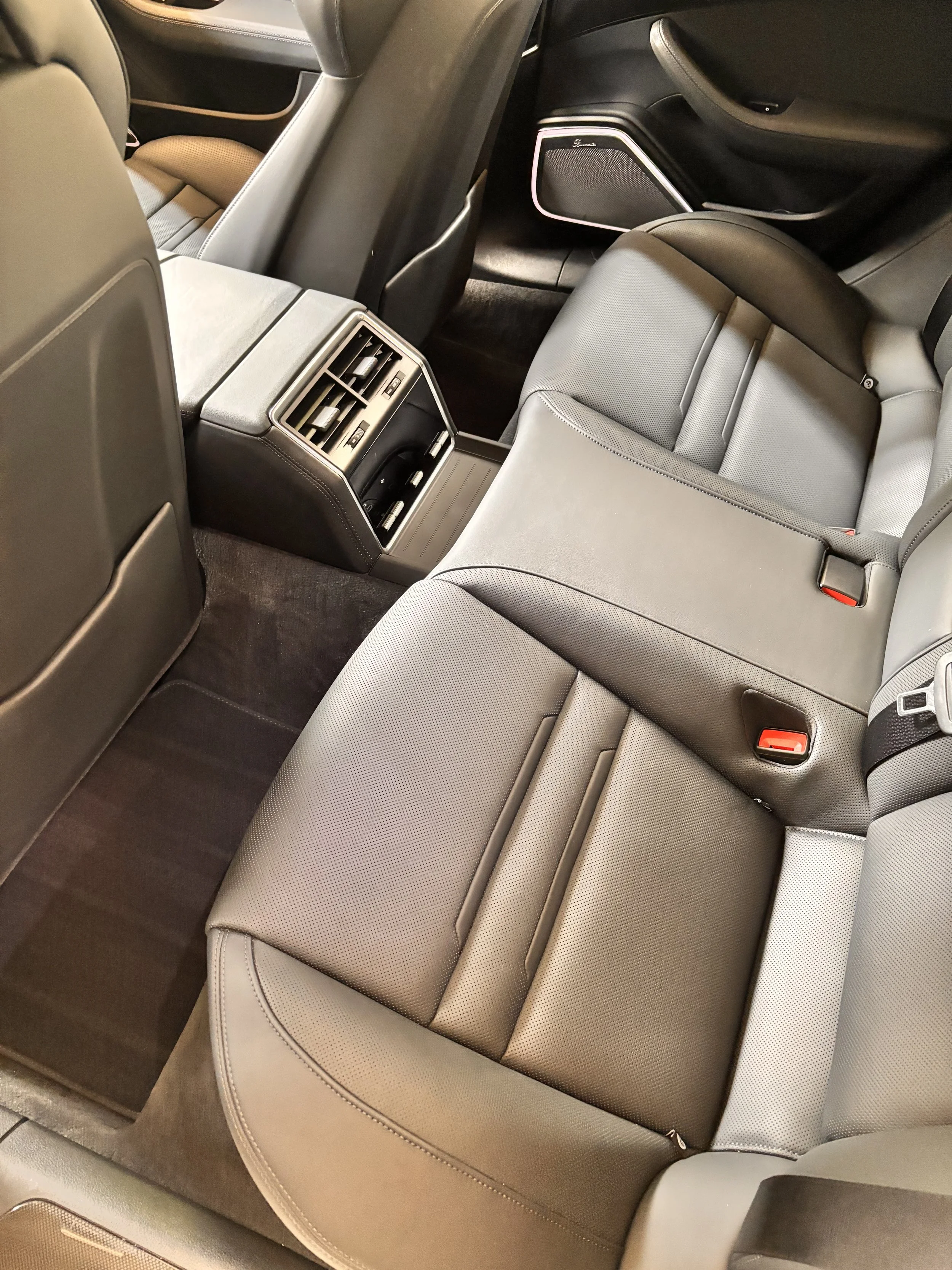 The interior of a modern vehicle showing the back seats, center console with air vents, and floor mats.