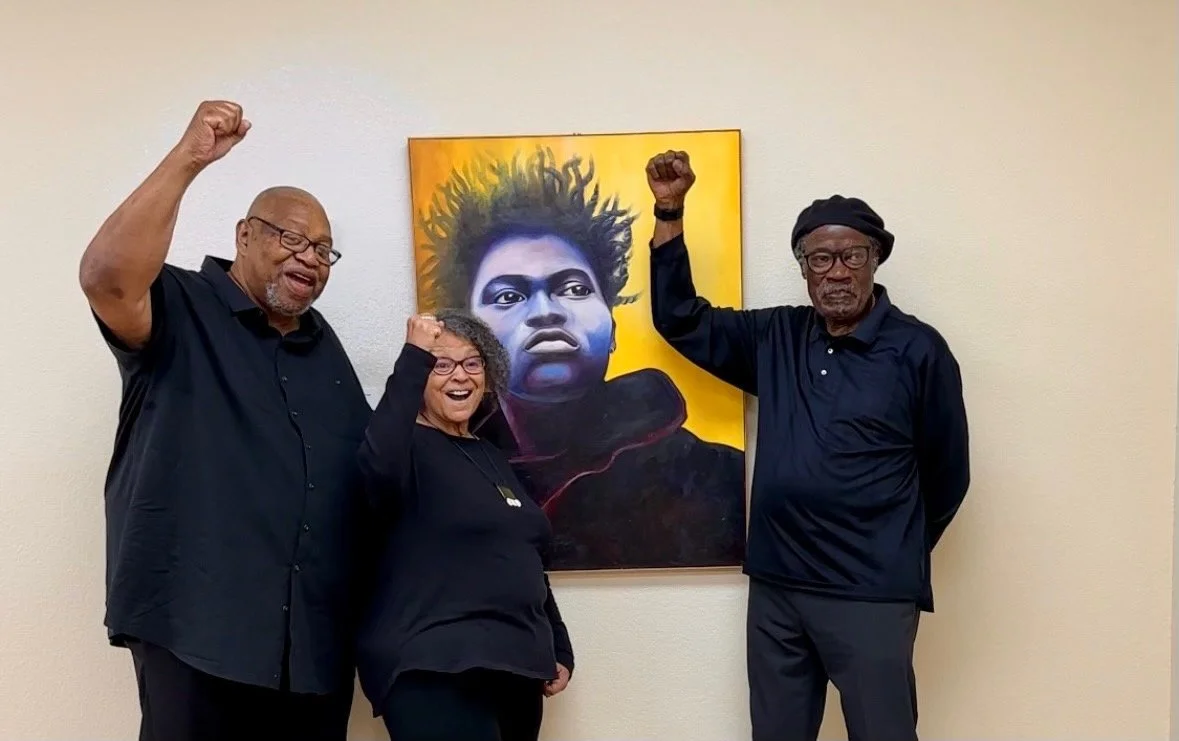Three people standing in front of a colorful portrait of singer and songwriter Tracy Chapman, raising their fists in celebration.