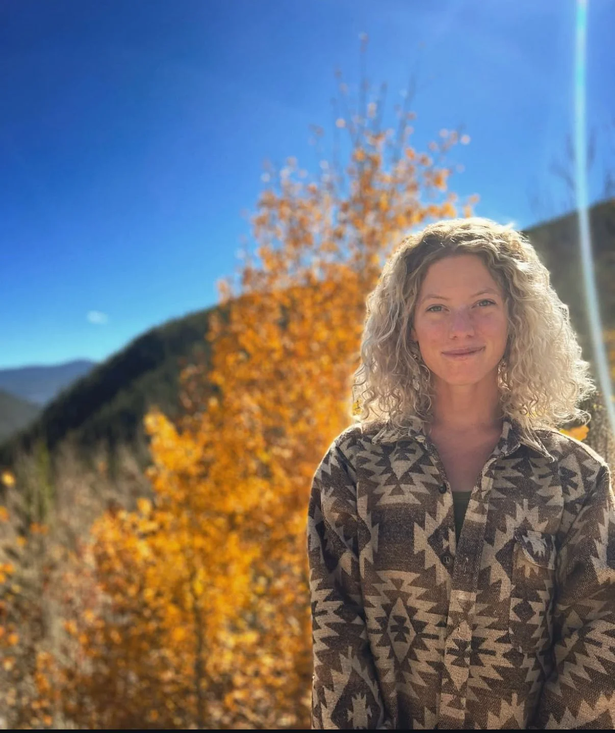 Tess Harris, trauma and EMDR therapist in Evergreen, Colorado, smiling outdoors among autumn trees with mountains in the background.