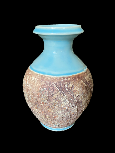 A ceramic vase with a textured, crackled beige lower half and a smooth, light blue upper half against a black background.