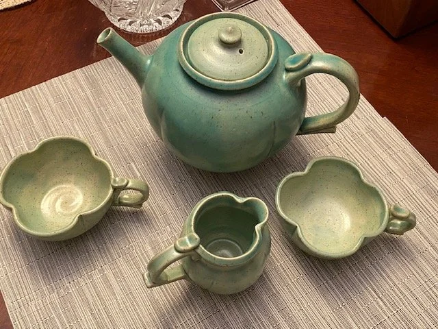 Green ceramic teapot with three matching cups on a woven placemat.