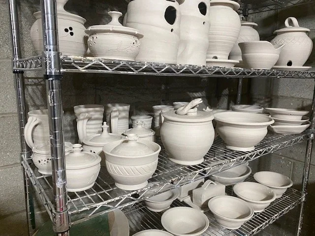 White ceramic pottery and bowls on metal wire shelves in a storage room.