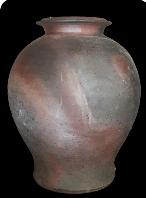 Ancient clay vessel with a rounded body and narrow opening at the top against a black background.