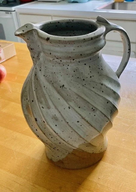 Ceramic pitcher with a leaf-shaped design on a wooden table.