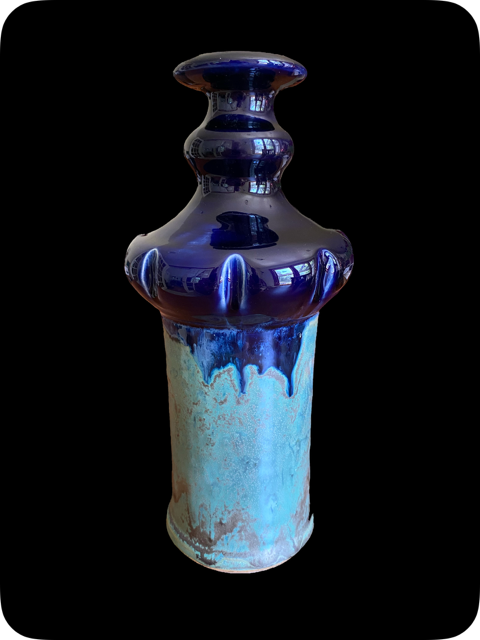 A ceramic vase with a dark blue, glossy, and textured top and a glazed base with a mix of blue and beige colors, against a black background.