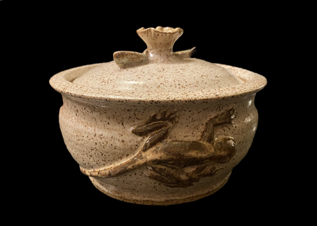 Cream-colored ceramic vessel with a lid, decorated with a raised dragon figure on the side, against a black background.