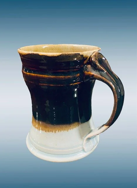 Ceramic mug with a handle, glazed in dark brown and light beige colors.