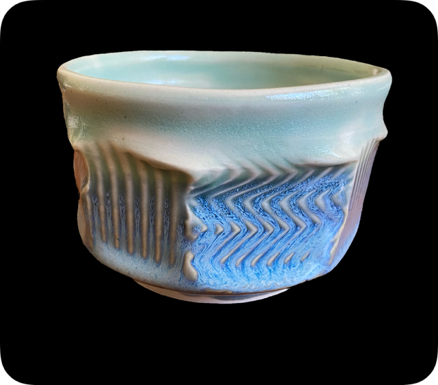 Ceramic bowl with textured design in cream and blue, set against a black background.