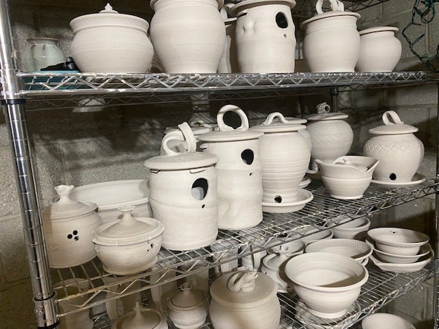 White unglazed ceramic pottery and cookware on metal shelving, including pots, bowls, and containers with lids.