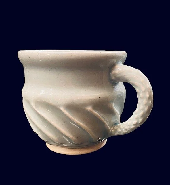A white ceramic cup with a textured handle and swirling design on the outside, set against a dark background.