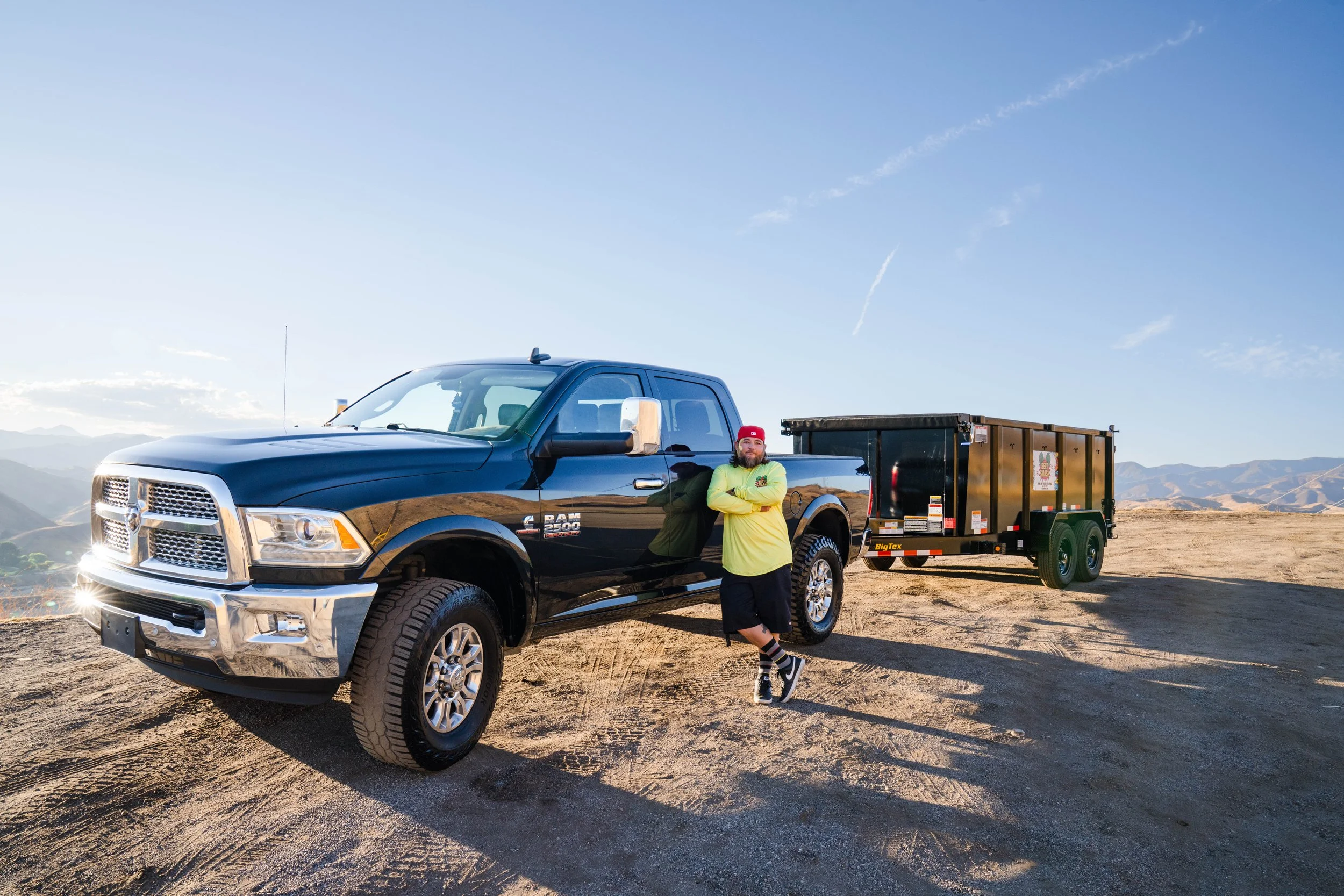 Owner of junk removal services for contractors in Santa Clarita posing next to his black trailer which is lifted and ready.