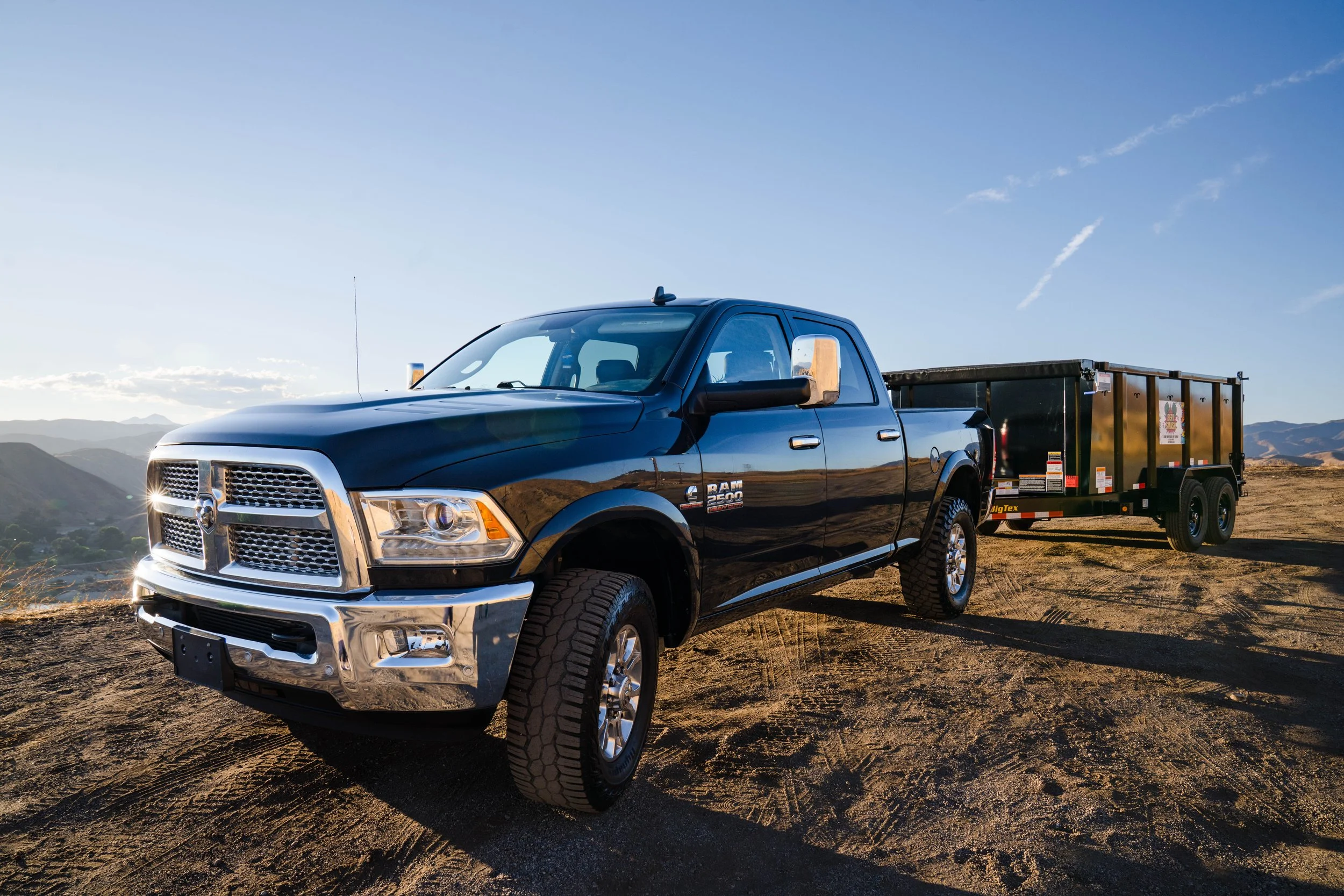 Black dodge RAM towing a black truck trailer with the view of the Santa Clarita Valley and Castaic behind it.