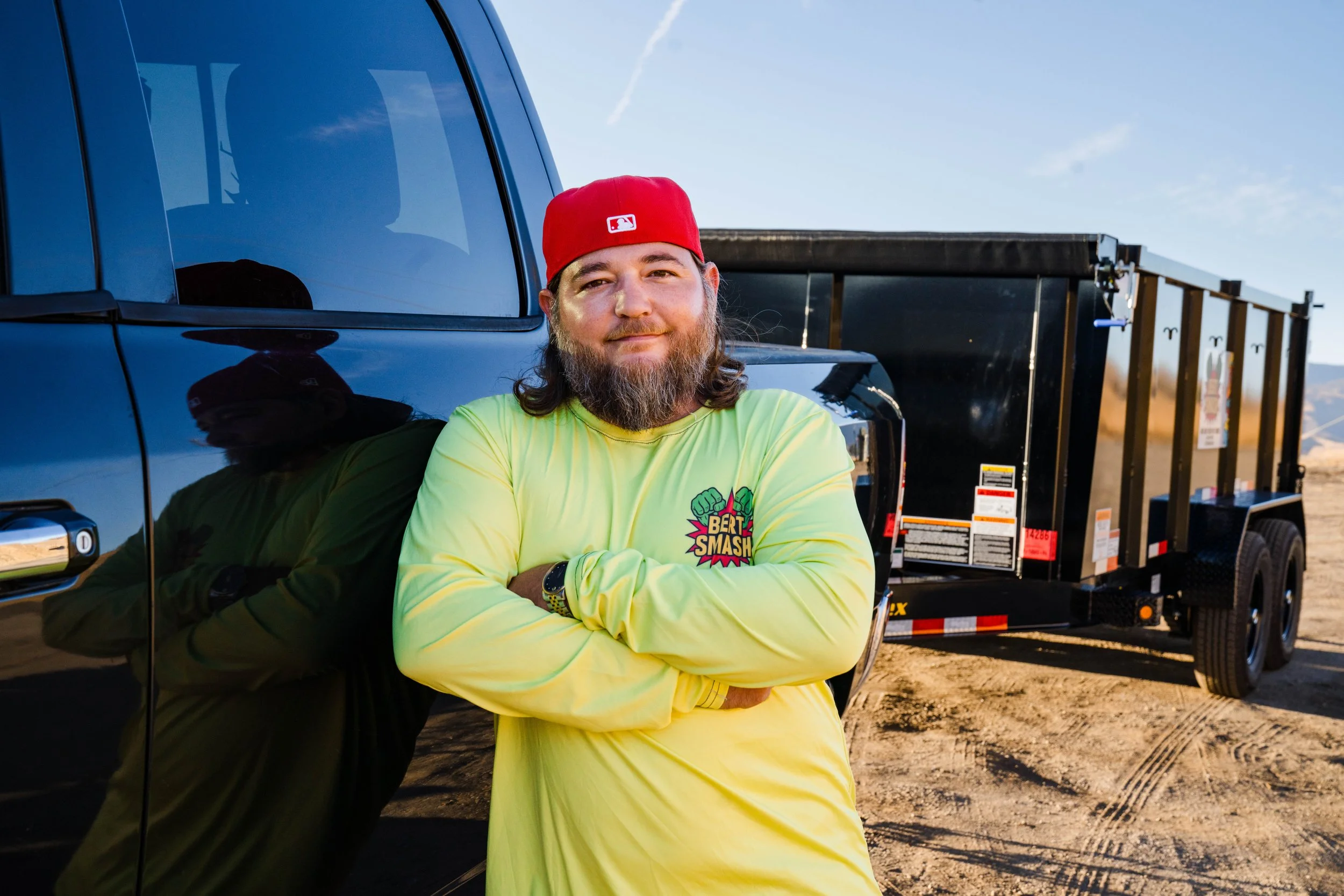 Owner of waste disposal services in Santa Clarita posing next to his black trailer.