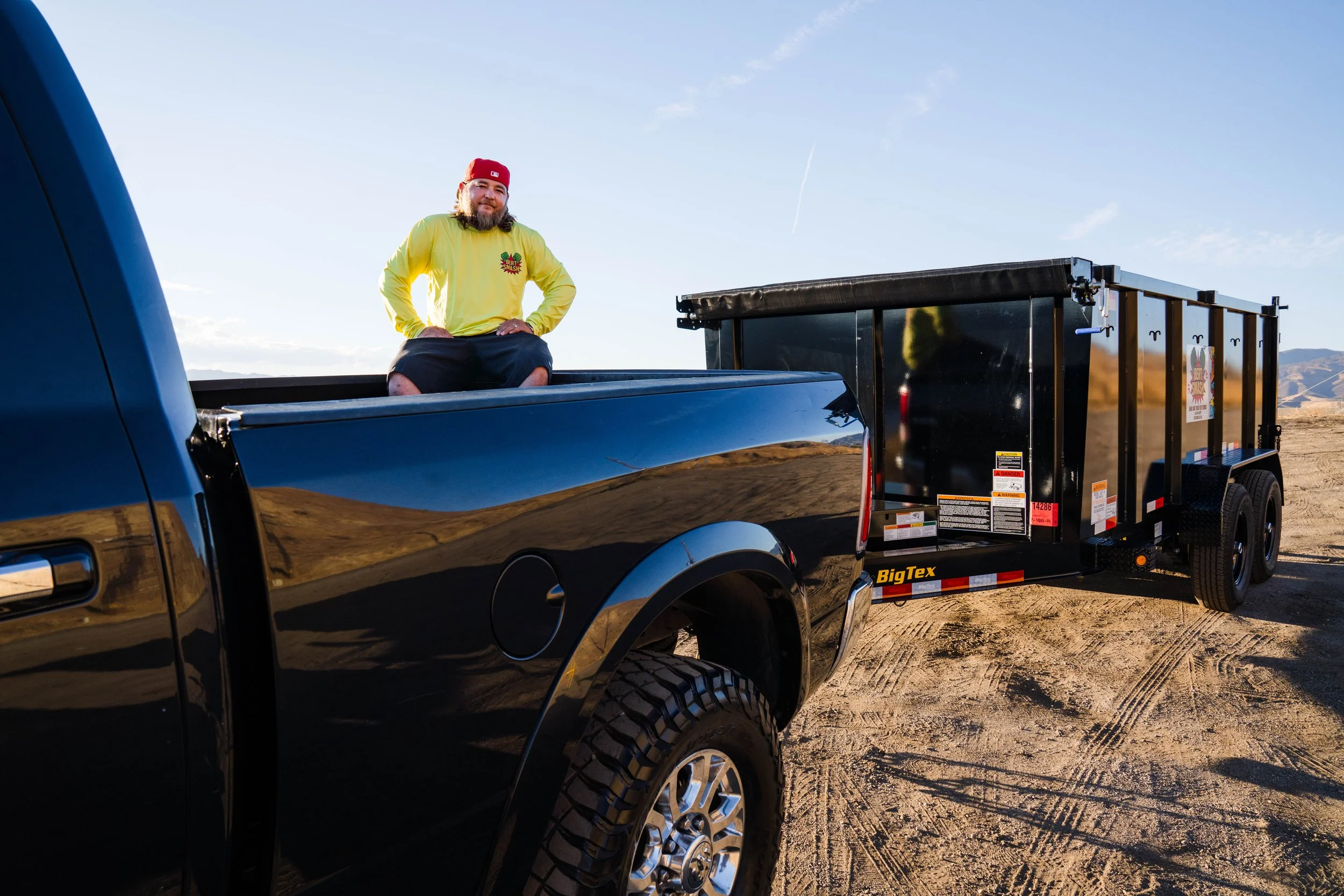 Owner of junk removal services for contractors in Santa Clarita posing next to his black trailer which is lifted and ready.