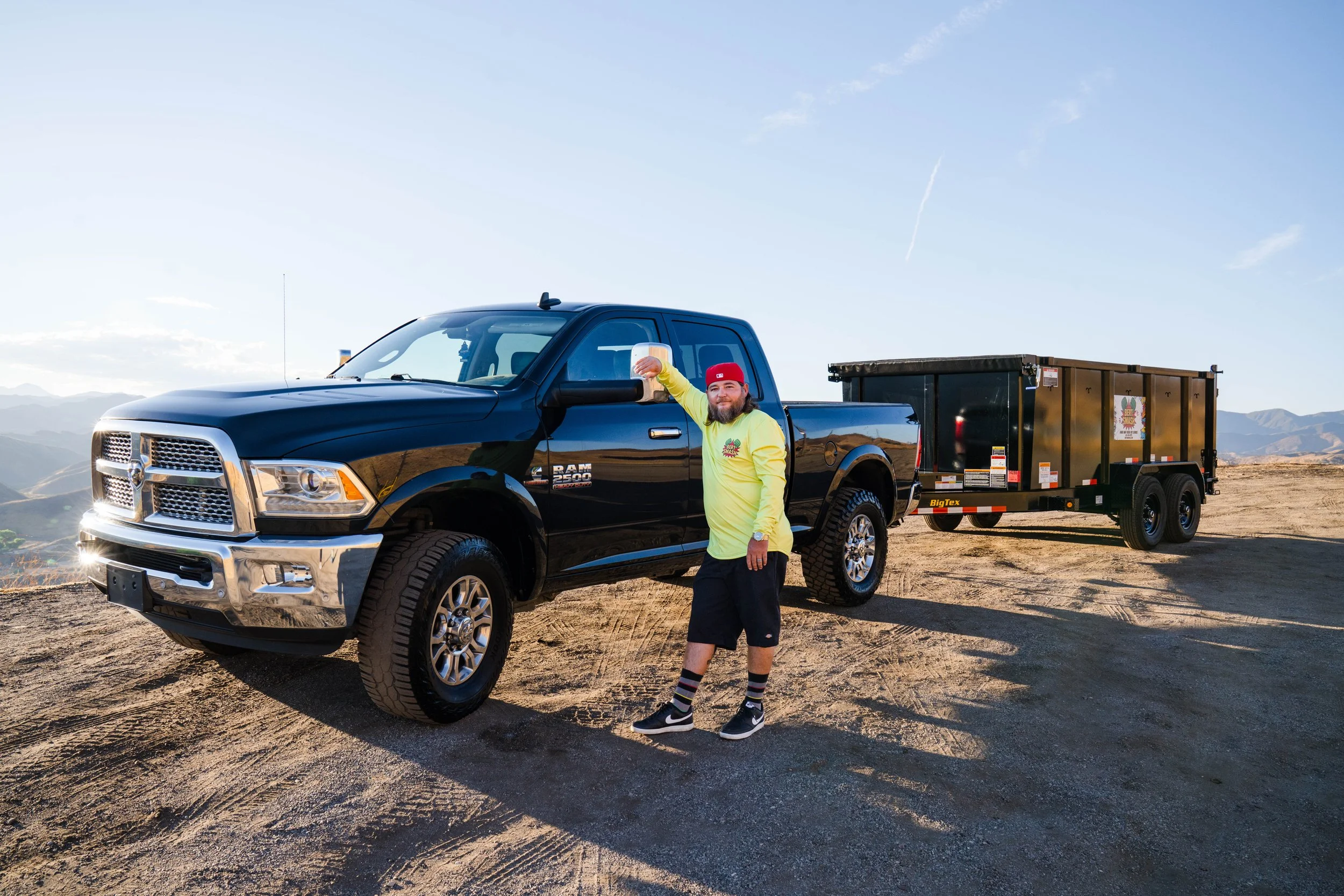 Owner of junk removal services for contractors in Santa Clarita posing next to his black trailer which is lifted and ready.