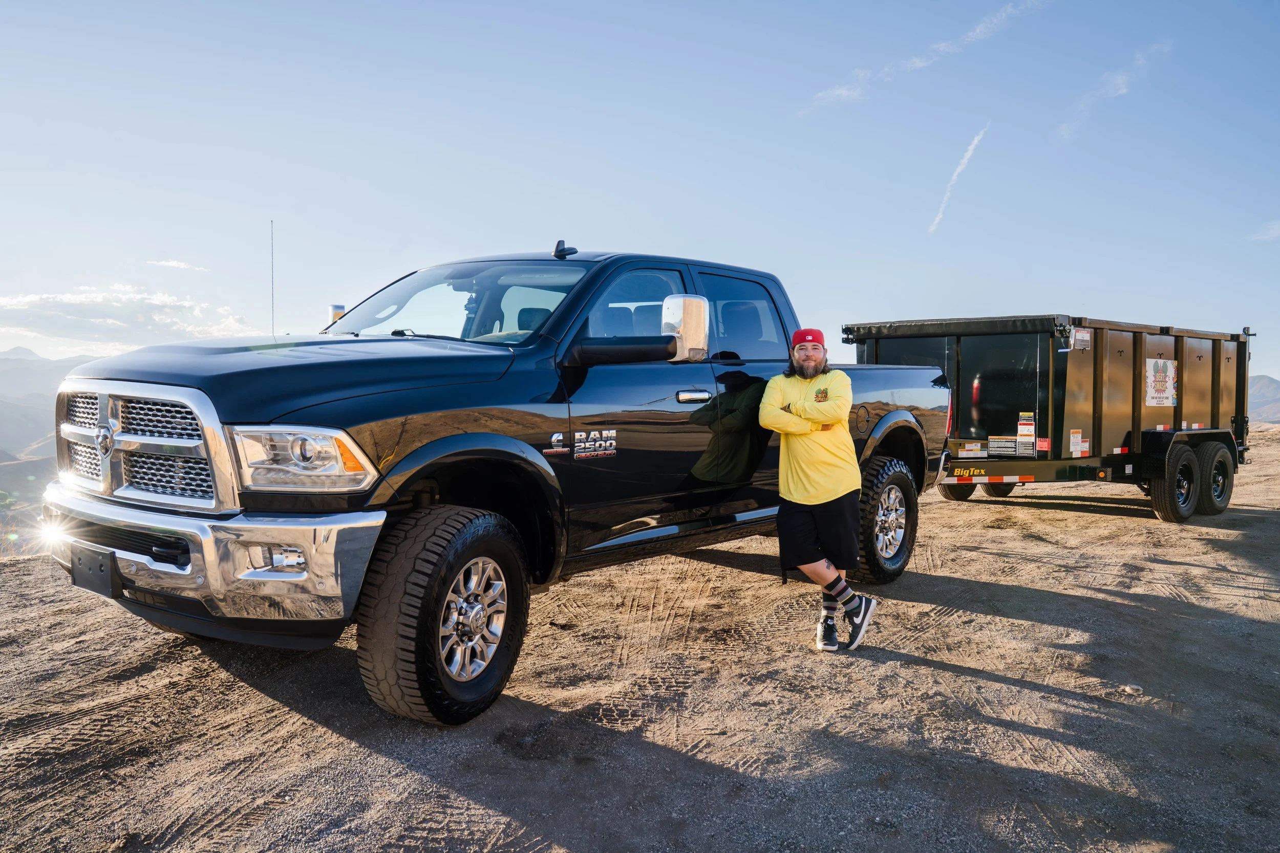 Owner of junk removal services for contractors in Santa Clarita posing next to his black trailer which is lifted and ready.