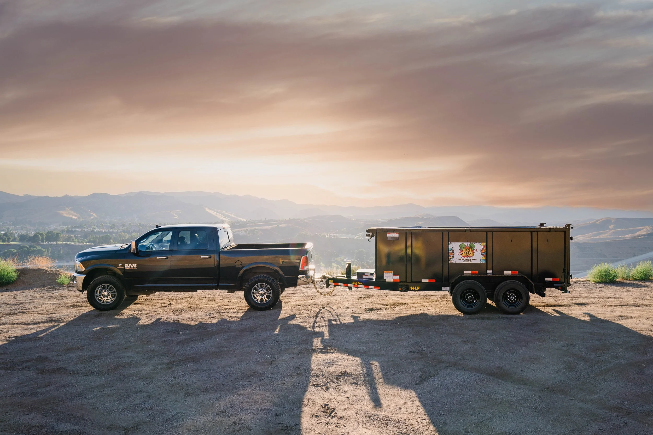 Black dodge RAM towing a black truck trailer with the view of the Santa Clarita Valley and Castaic behind it.