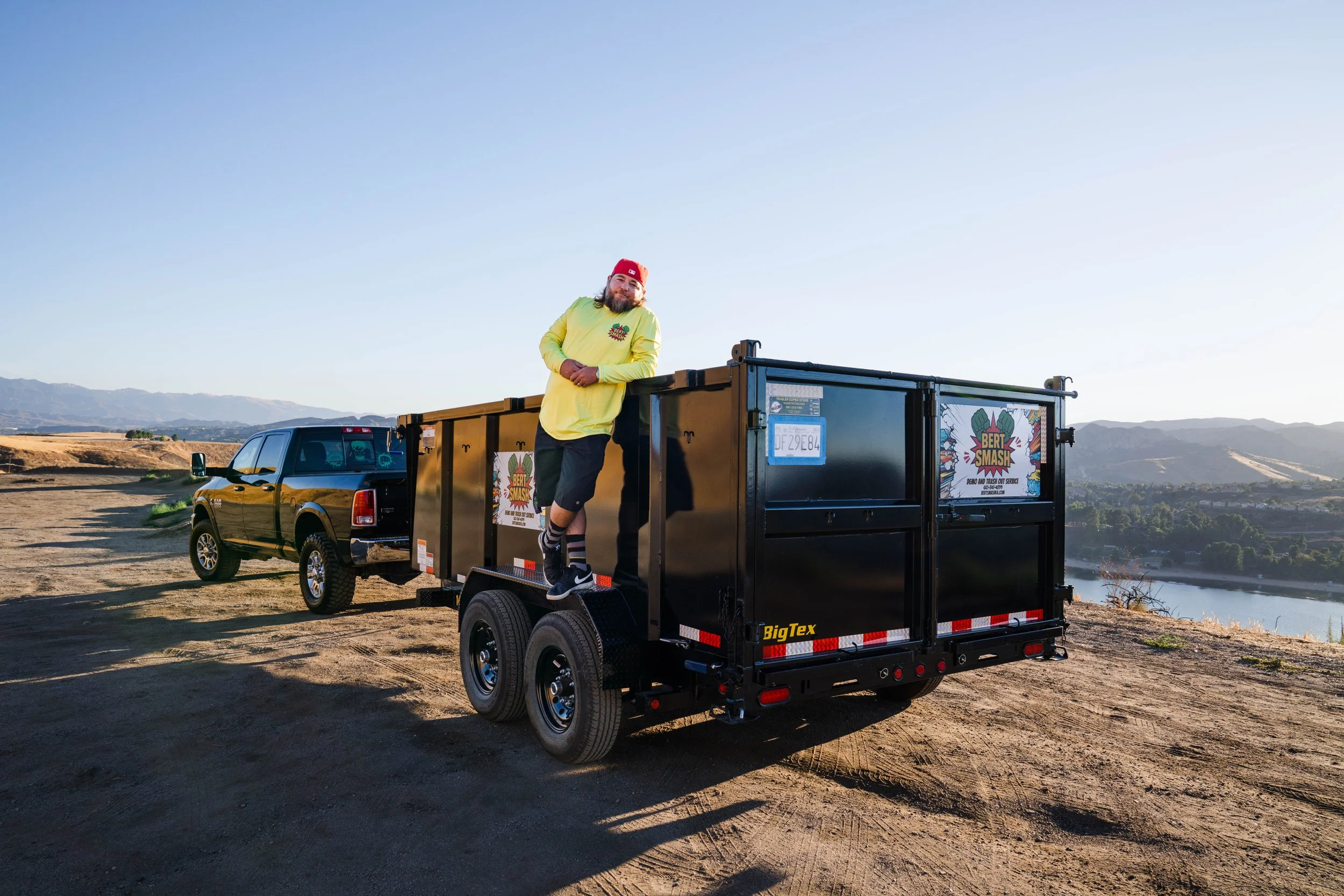 Owner of junk removal services for contractors in Santa Clarita posing next to his black trailer which is lifted and ready.