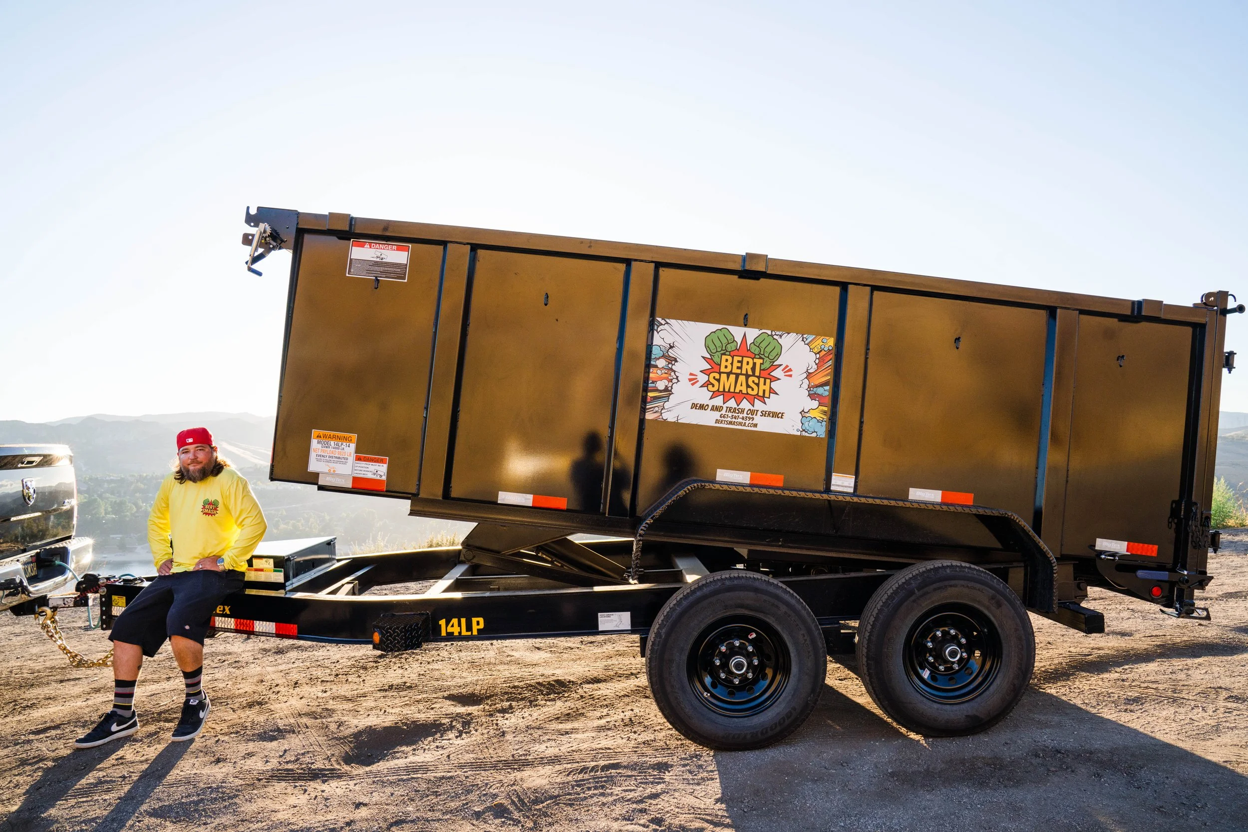 Owner of junk removal services for contractors in Santa Clarita posing next to his black trailer which is lifted and ready.