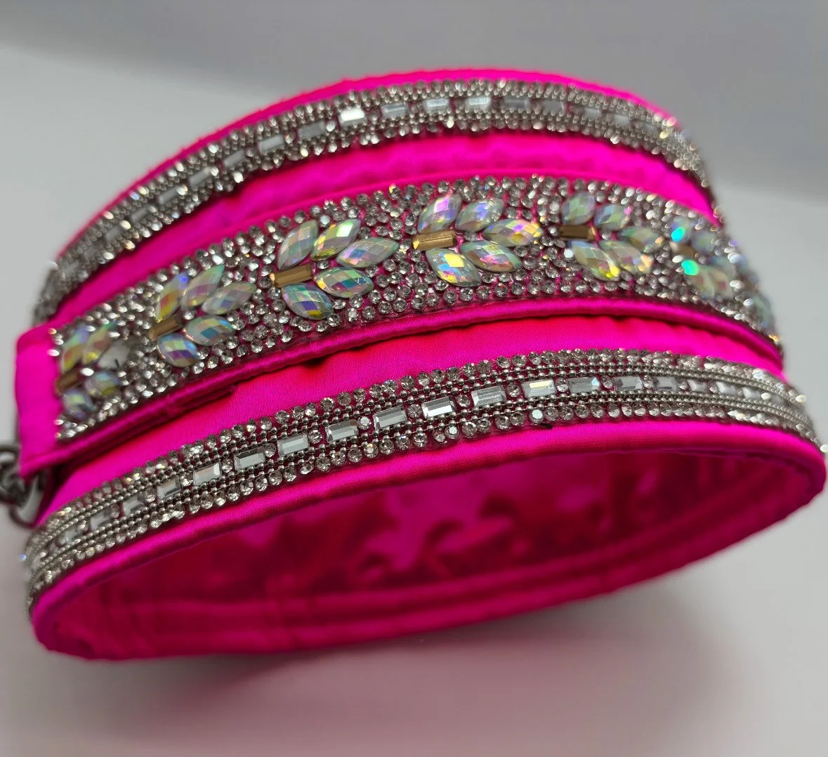 A bright pink fabric bracelet decorated with multiple rows of rhinestones and iridescent jewel embellishments.