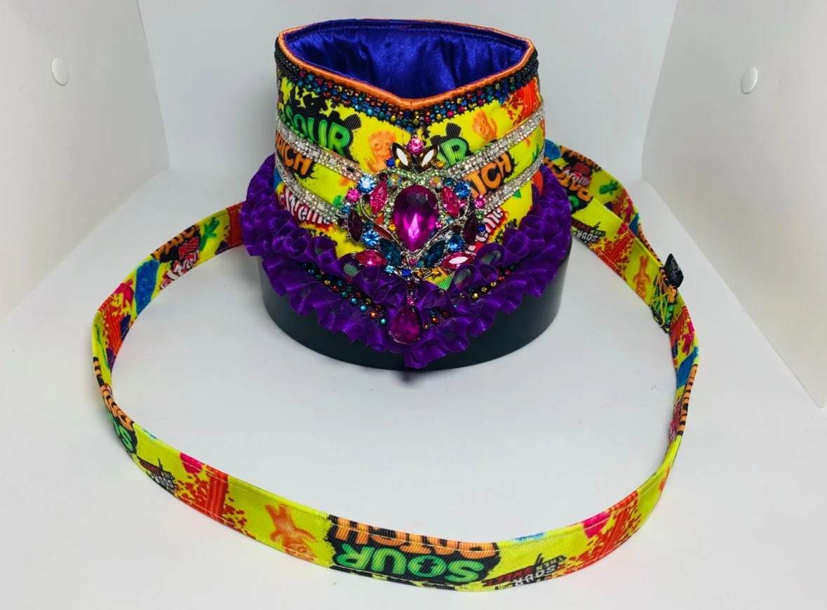 Colorful costume jewelry display including necklaces, a jeweled choker, and a colorful fabric belt on a black stand against a white background.