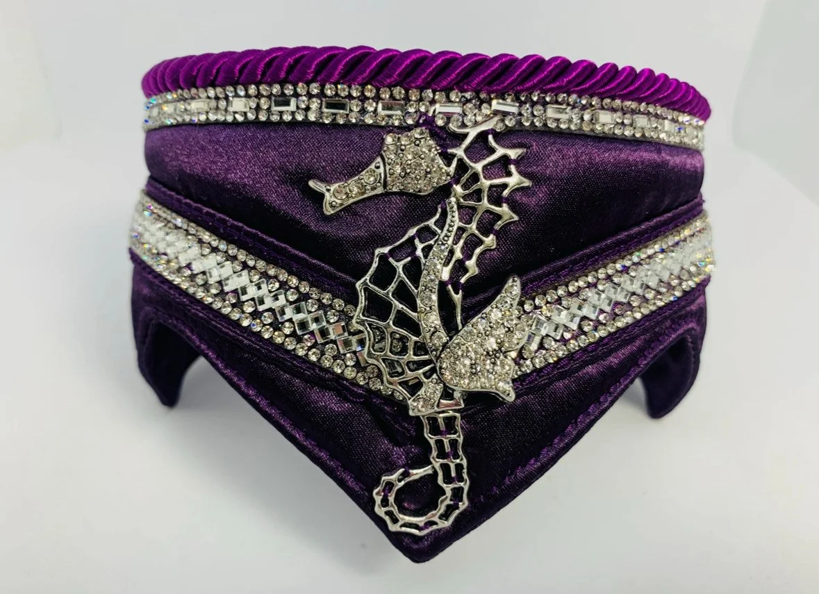 A purple velvet clutch purse decorated with rhinestones and a silver seahorse-shaped brooch.